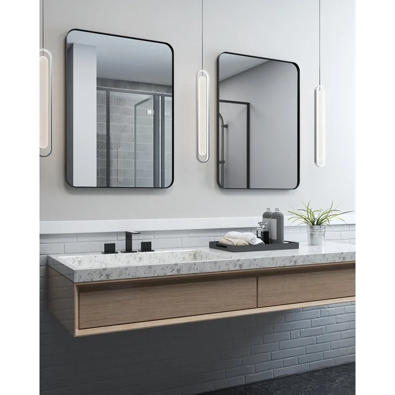 A modern bathroom vanity area with a wooden floating cabinet, a terrazzo-style countertop, two black-framed rounded mirrors, and vertical pendant lights.