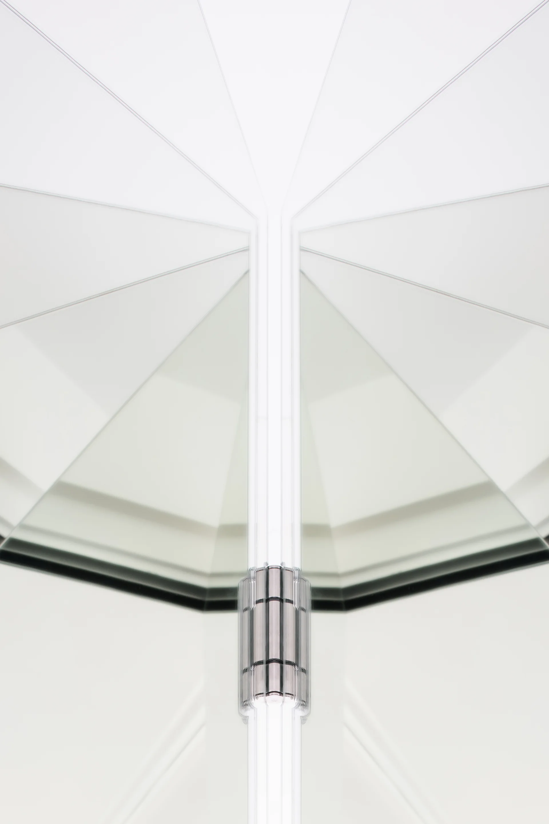A symmetrical close-up of a silver metal door hinge mounted between white reflective glass panels.