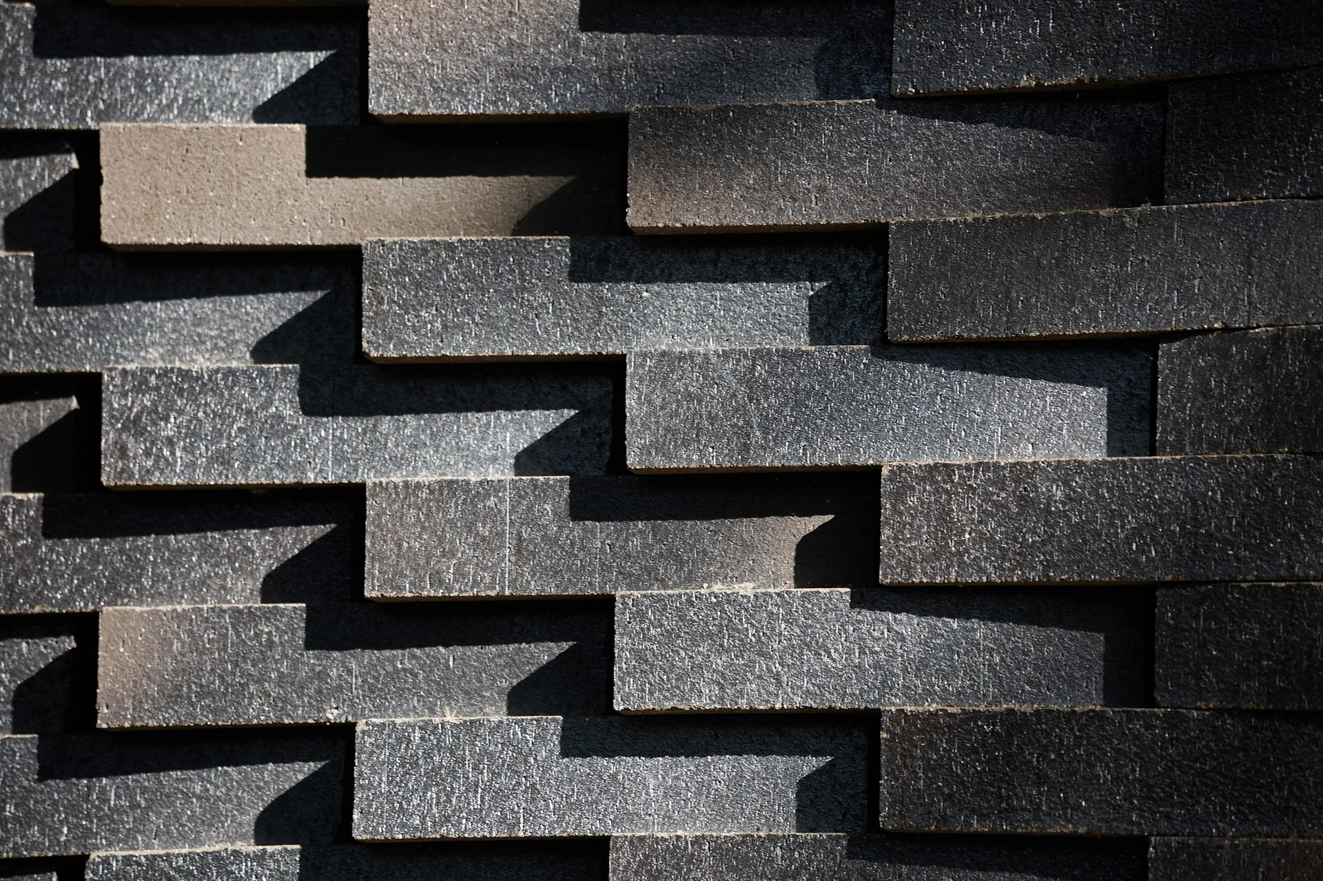 A close-up view of dark charcoal stone cladding with a staggered, layered block pattern creating deep dimensional shadows.