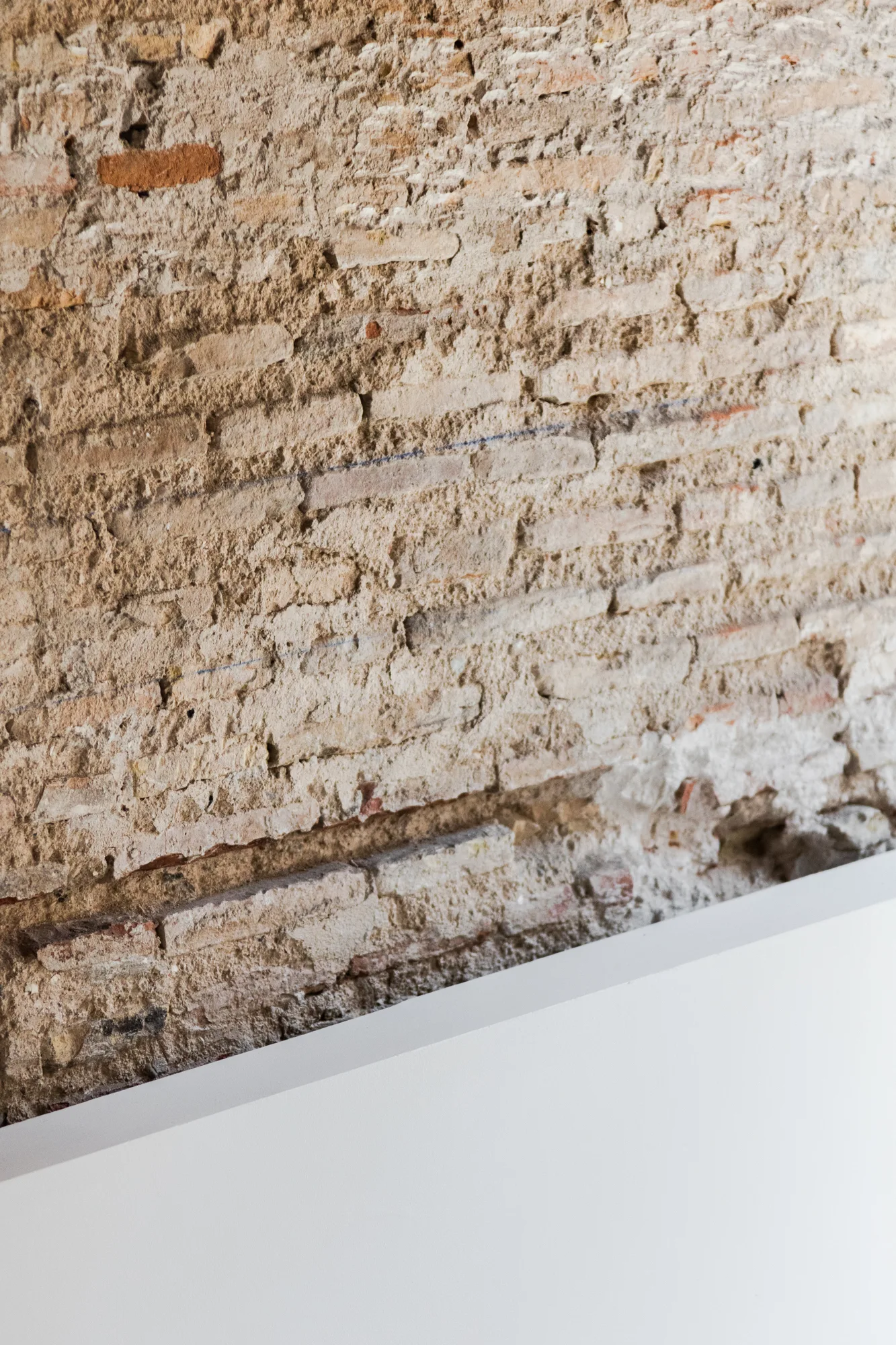 A close-up view showing a weathered, rough-textured brick wall meeting a smooth, matte white diagonal surface.