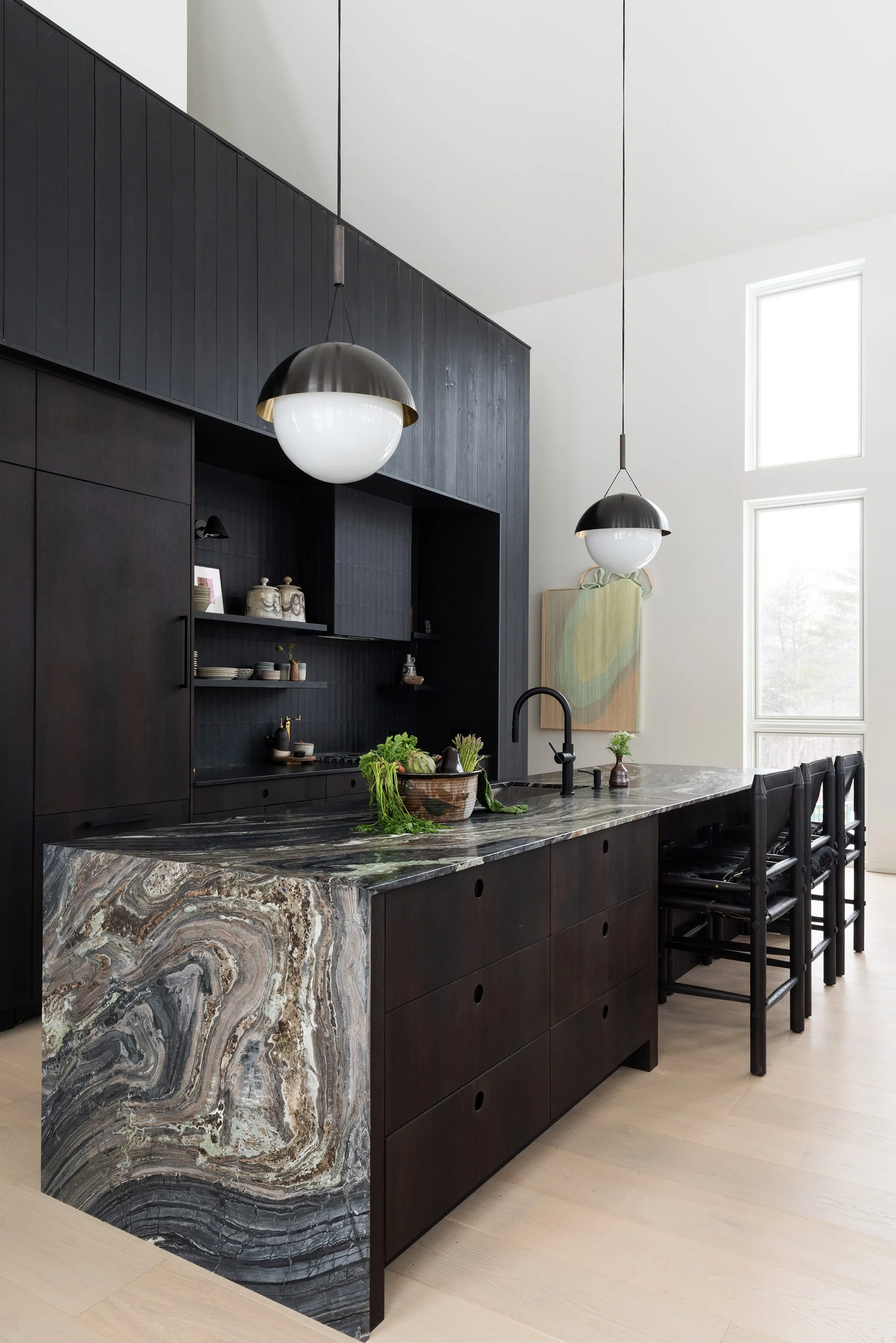 A modern kitchen featuring dark wood cabinetry, a large island with a swirling stone waterfall edge, and two dome pendant lights.