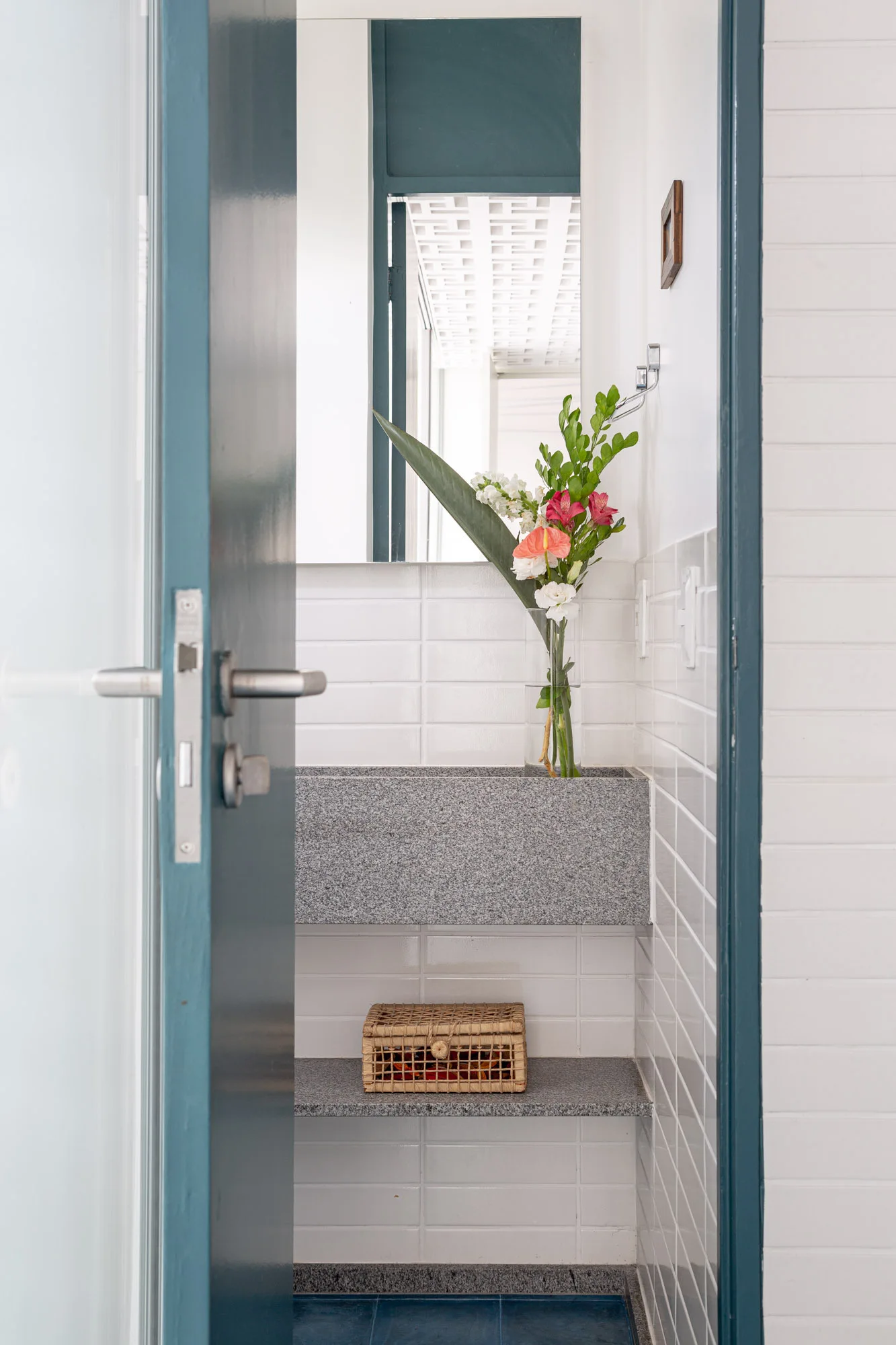 A bathroom viewed through a blue doorway features a floating grey stone sink and a matching lower shelf against white tiled walls.