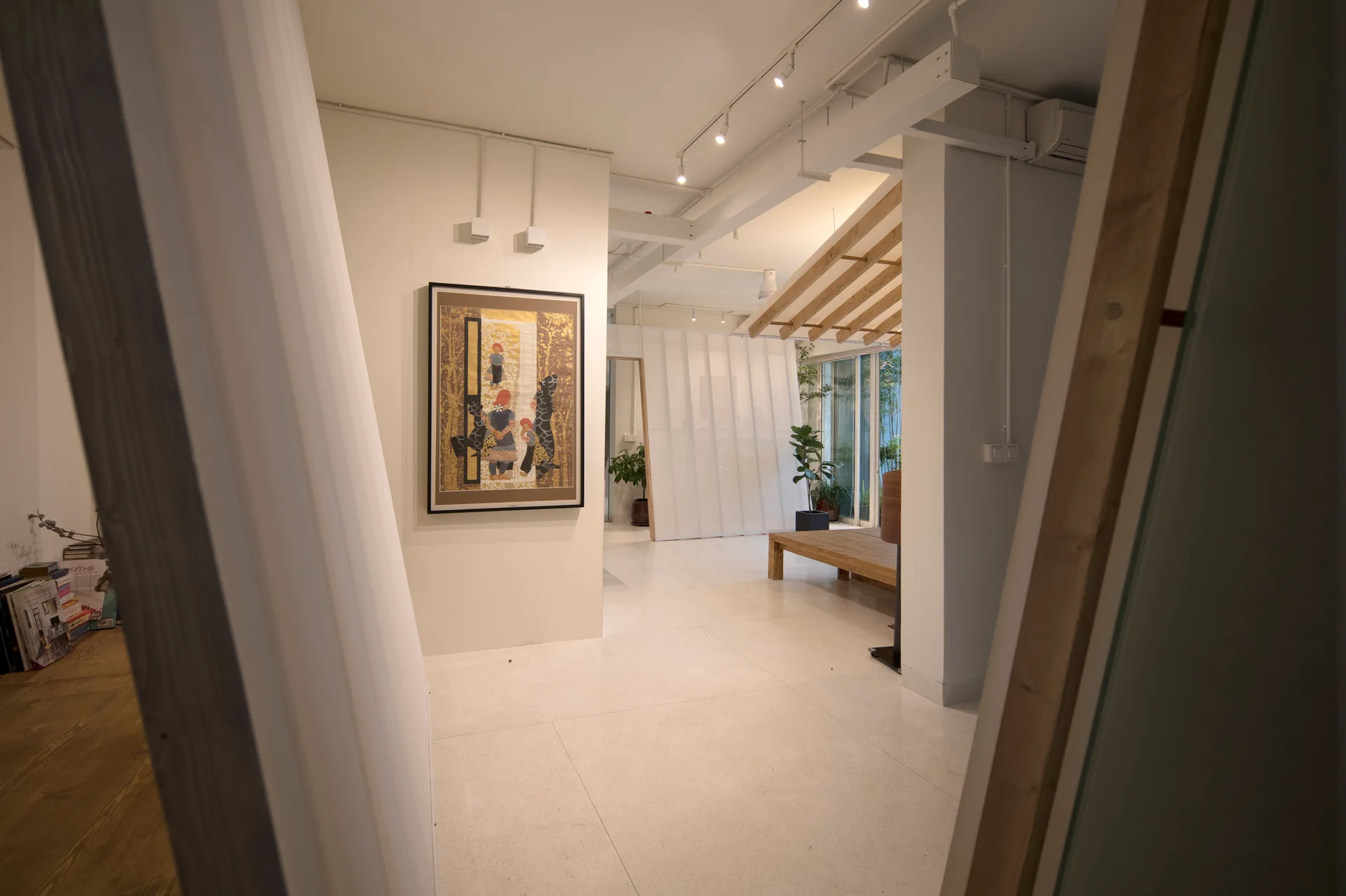A minimalist open interior features large white tile floors, a framed art piece on the wall, and a low wooden platform with an angled slatted roof.