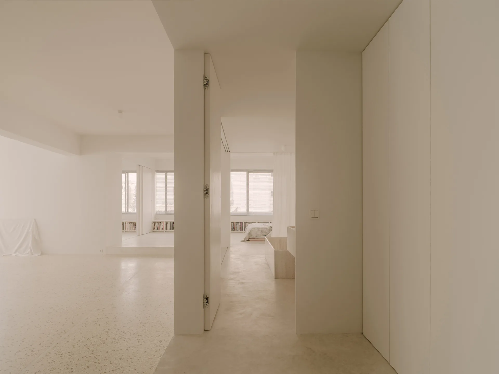 A minimalist beige bedroom interior with floor-to-ceiling cabinets, a low-profile bed, and light terrazzo flooring.