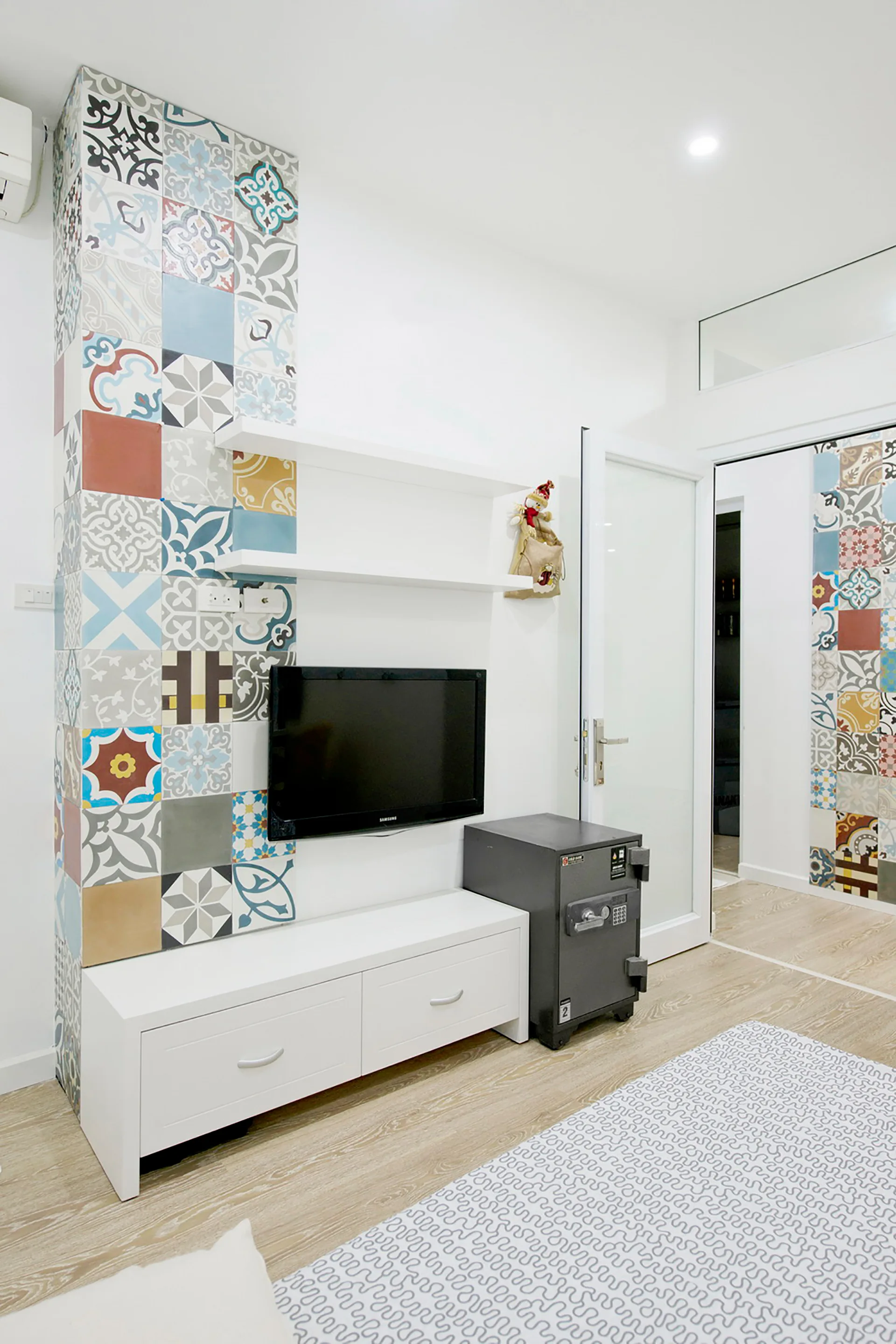 A modern white living space features a vertical column clad in multicolored patterned tiles next to a wall-mounted TV and a low white media console.