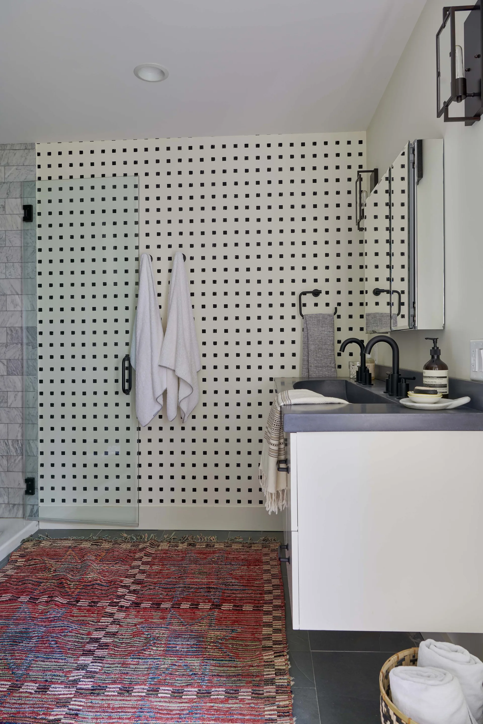 A modern bathroom features a white vanity with matte black faucets against a black and white dotted wallpaper background.