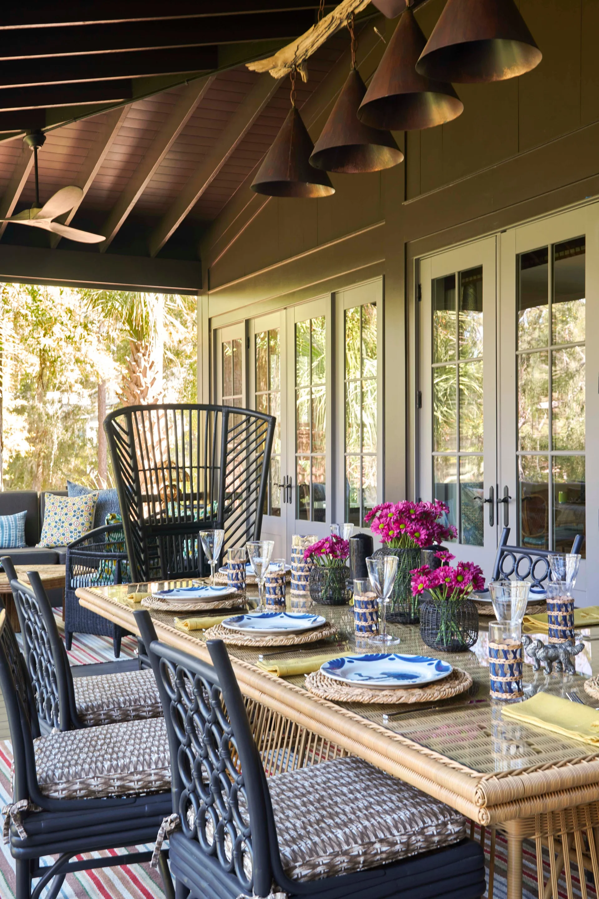 A covered outdoor porch features a glass-topped dining table set with blue and white plates, woven placemats, and black patterned chairs.