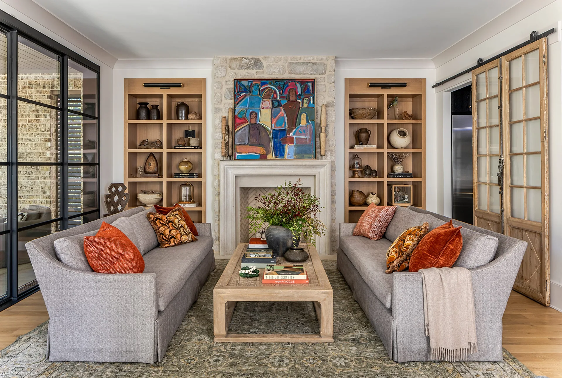Symmetrical living room featuring two gray sofas facing each other, a central stone fireplace, and custom oak bookcases on either side.