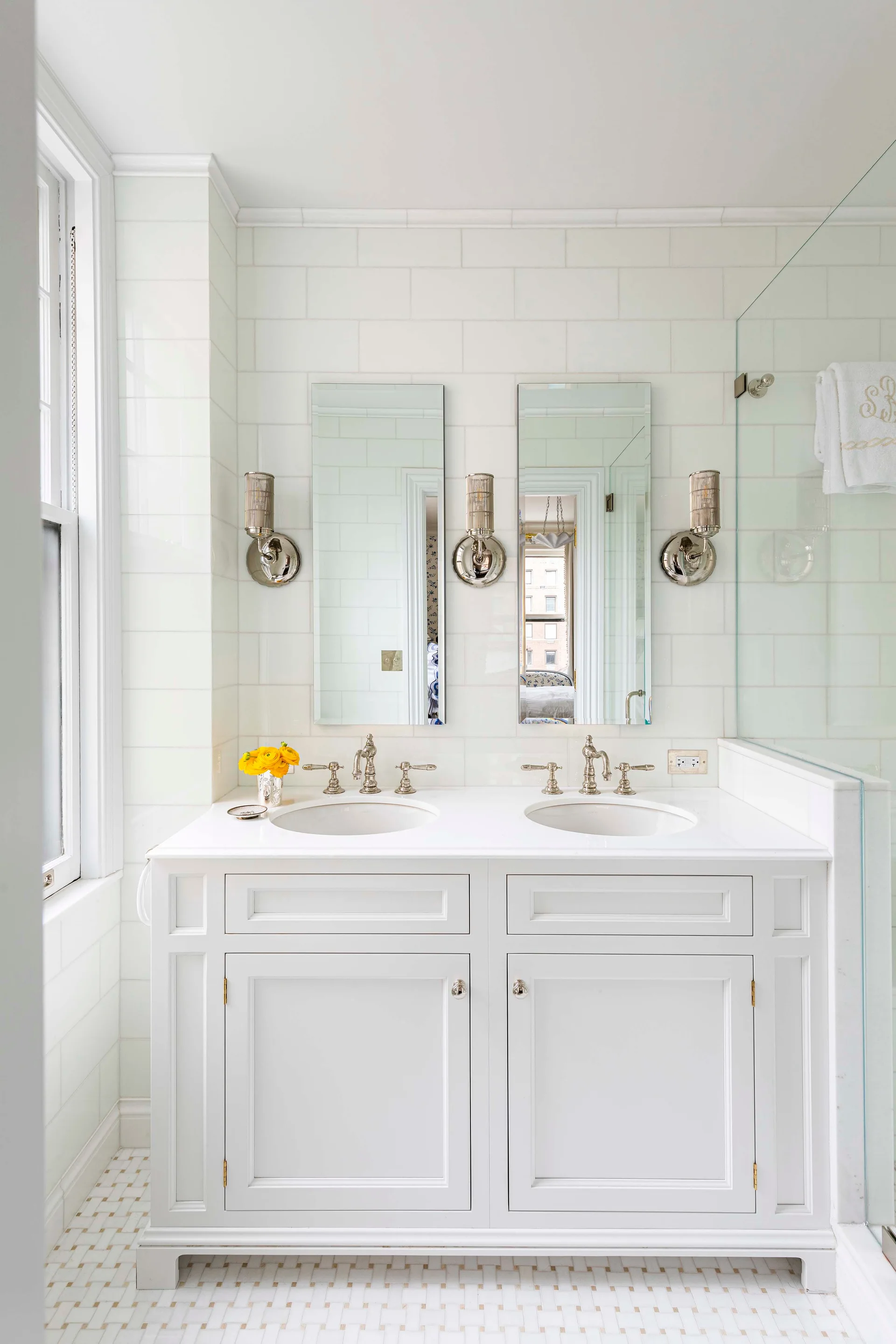 A bright white bathroom with a double sink vanity, twin rectangular mirrors, polished silver sconces, and a subway tile backdrop.
