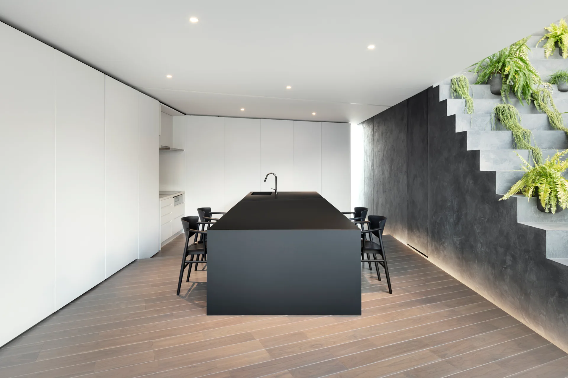 A central matte black kitchen island is surrounded by chairs opposite a textured gray staircase decorated with cascading green plants.