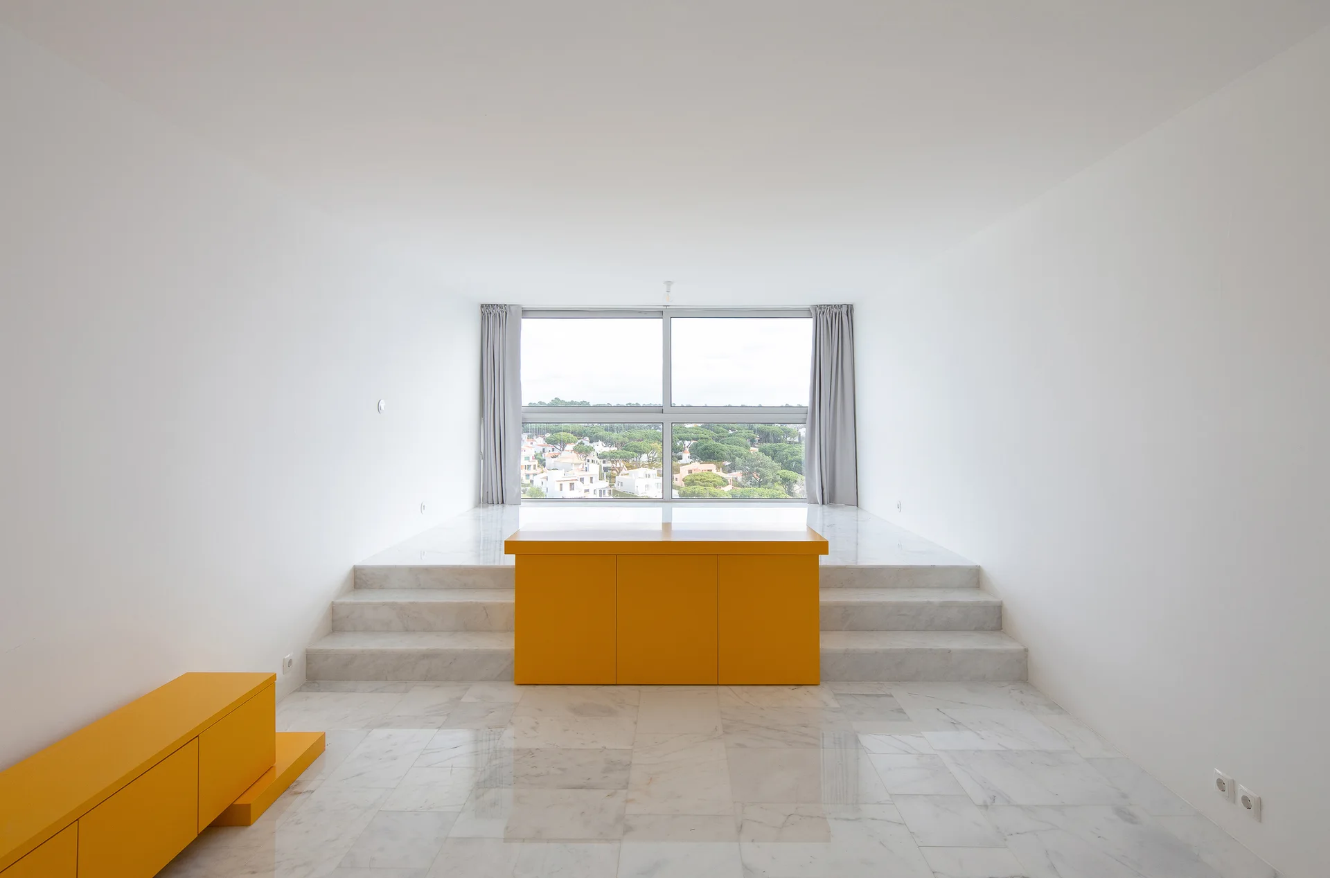 A minimalist room with polished white marble flooring features steps leading to a raised platform and a bright yellow cabinet.