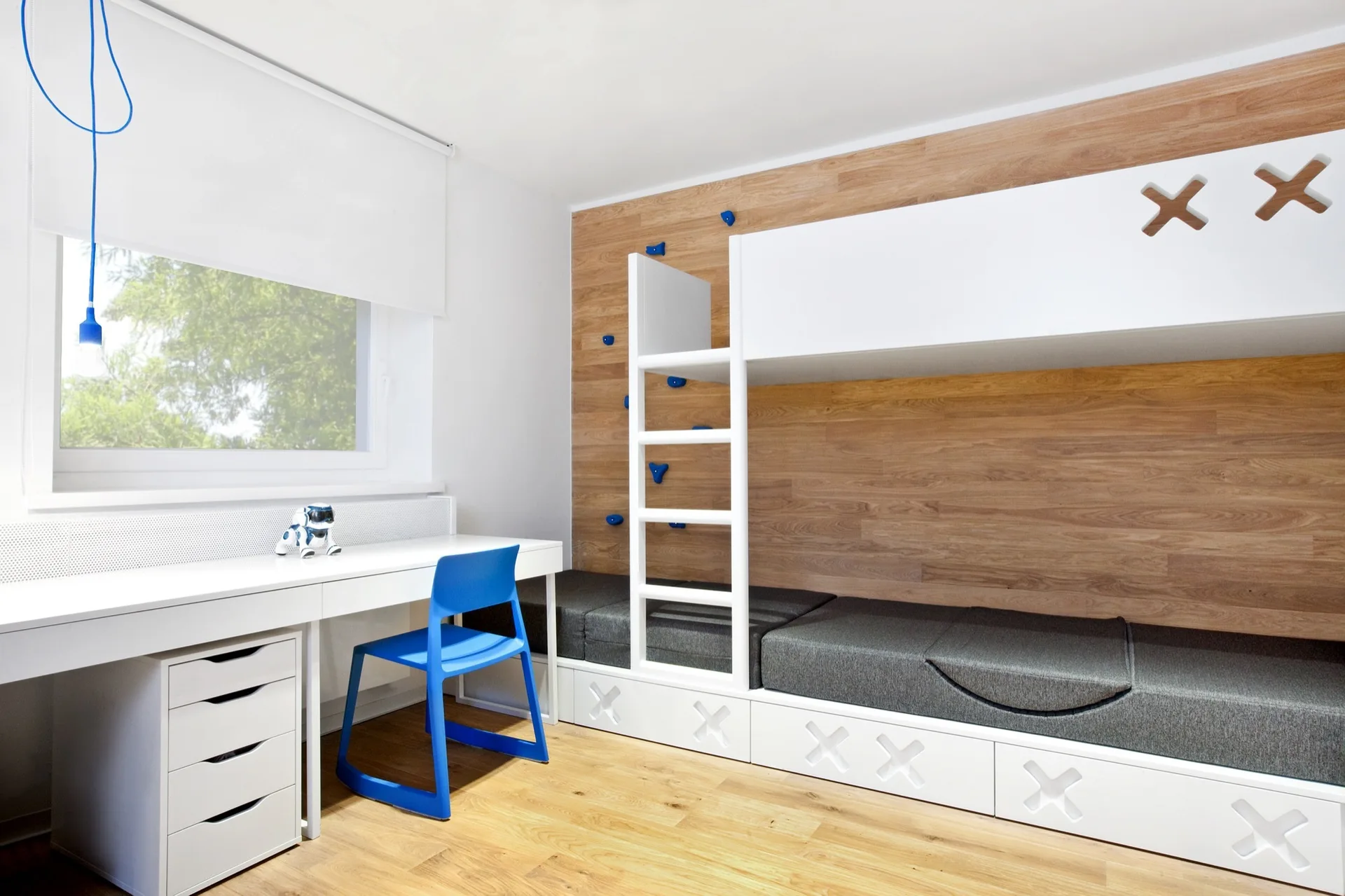 A modern children's bedroom features a built-in white bunk bed with climbing holds on a wood-paneled wall and an adjacent white study desk.