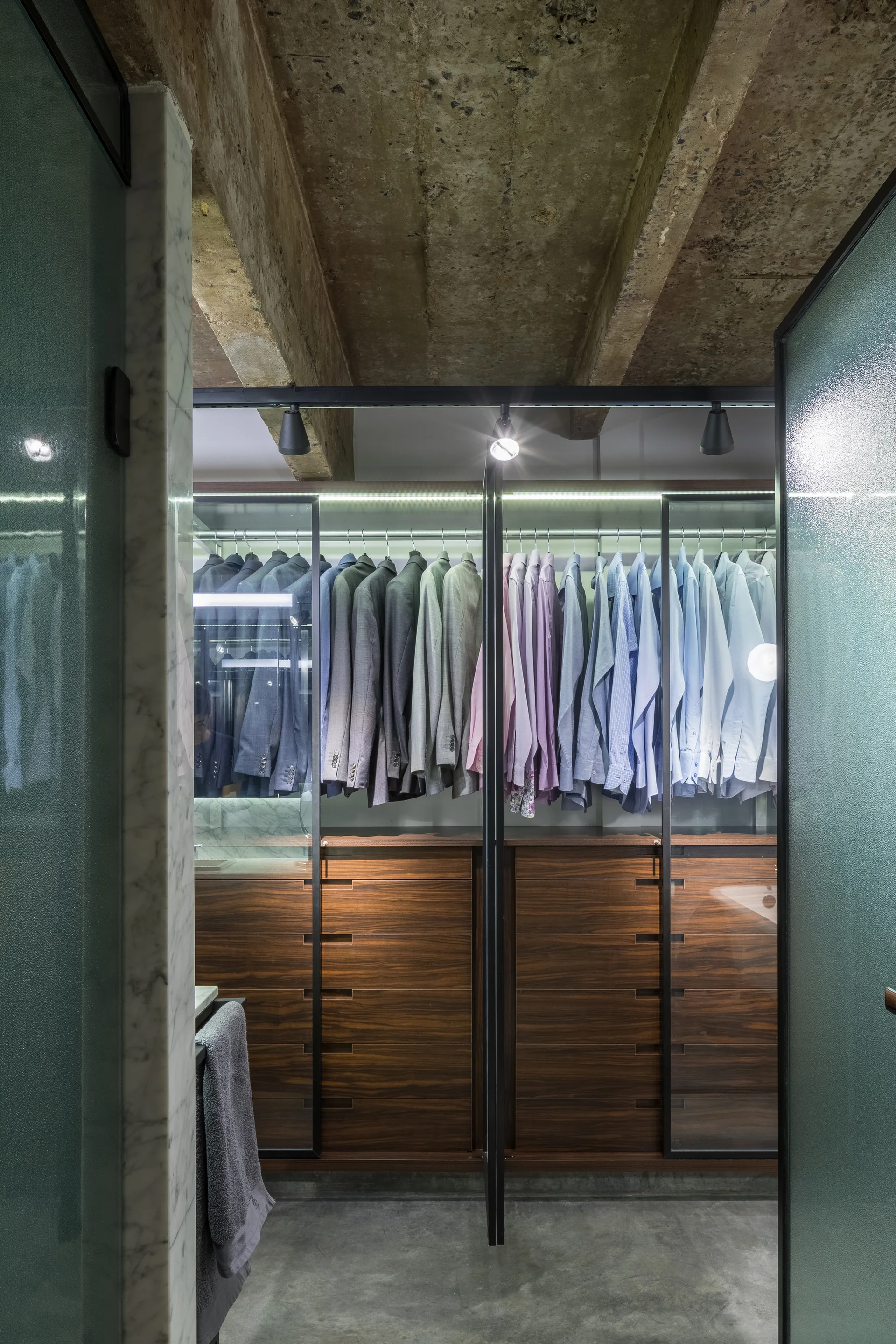 A modern walk-in closet with dark wood drawers and organized clothing beneath an exposed concrete ceiling.