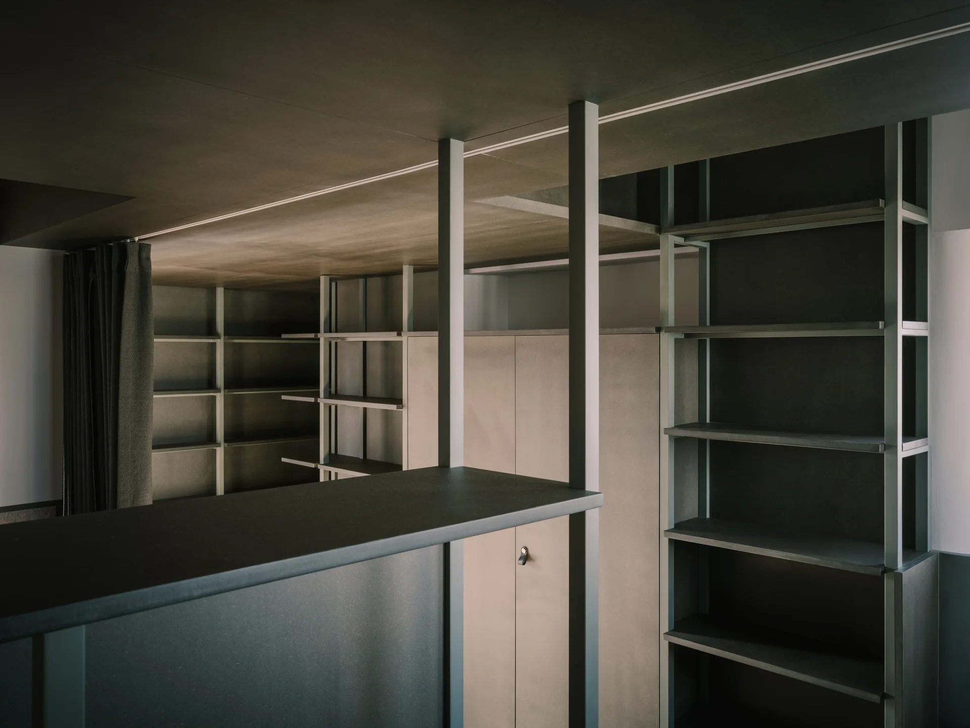 A minimalist dark charcoal grey custom closet storage system featuring multiple open shelves, a central cabinet, and matte black structural support posts.