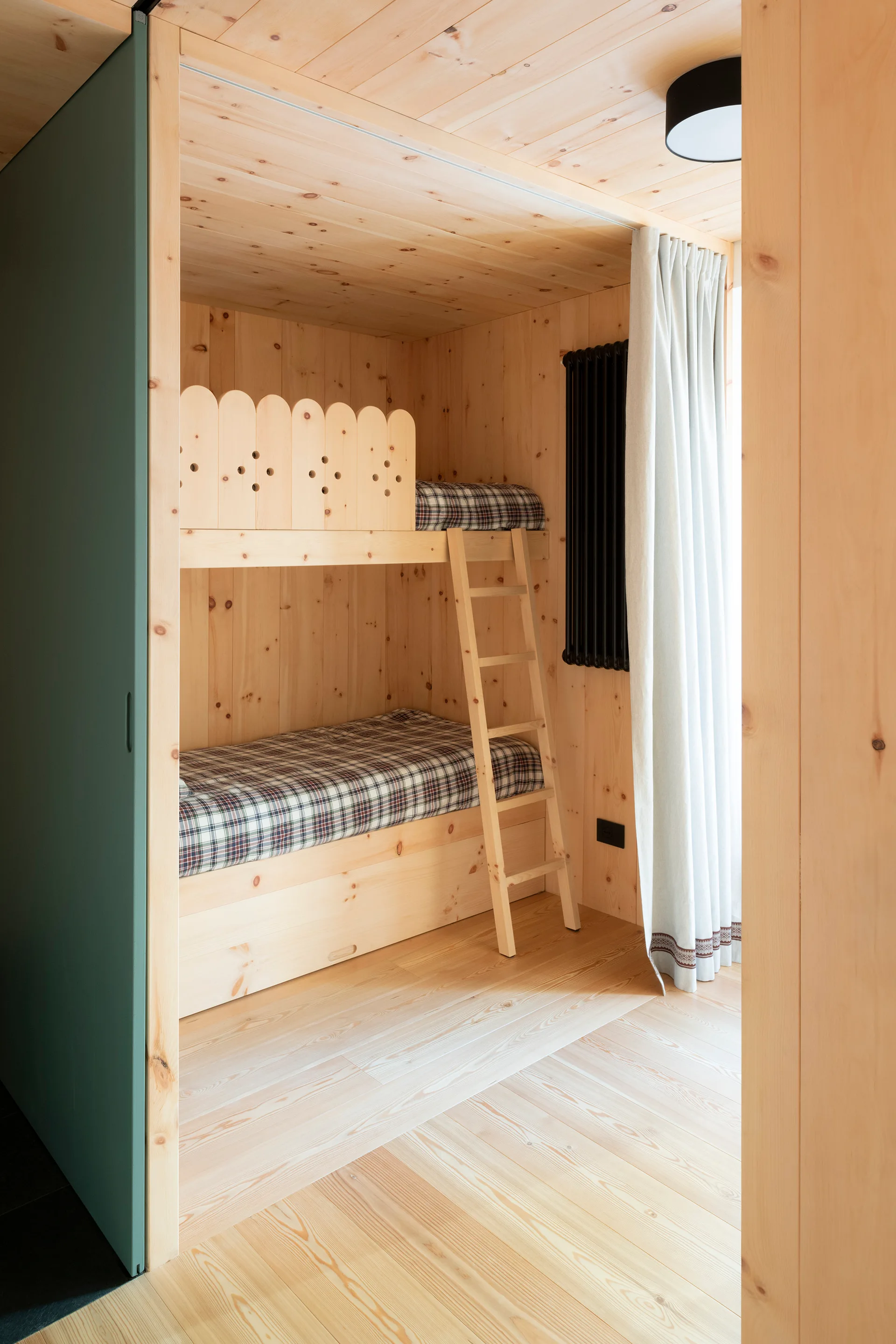 A small bedroom alcove featuring built-in wooden bunk beds, a ladder, a green sliding door, and knotty pine paneling on the walls and ceiling.