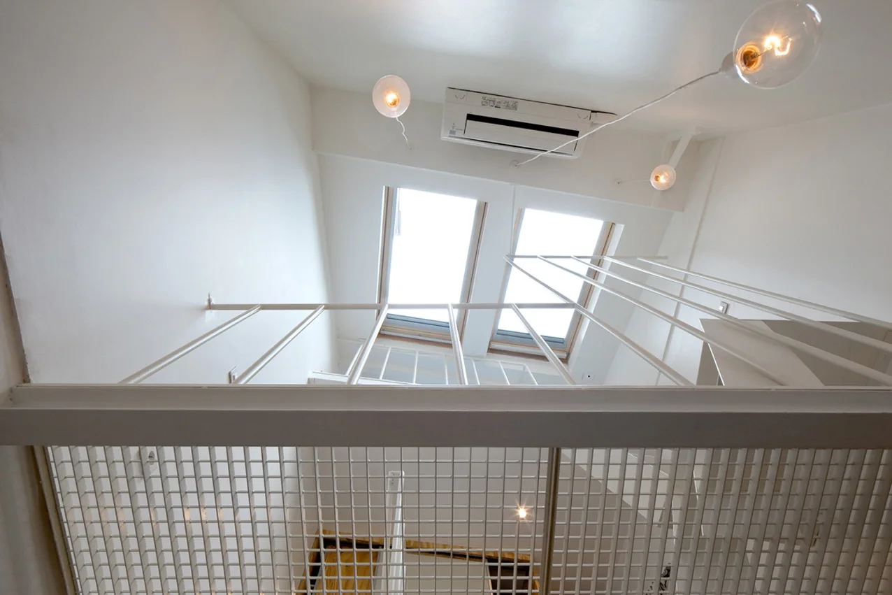 A low-angle view looking up a white minimalist stairwell with a metal grid railing towards two skylights and globe pendant lights.