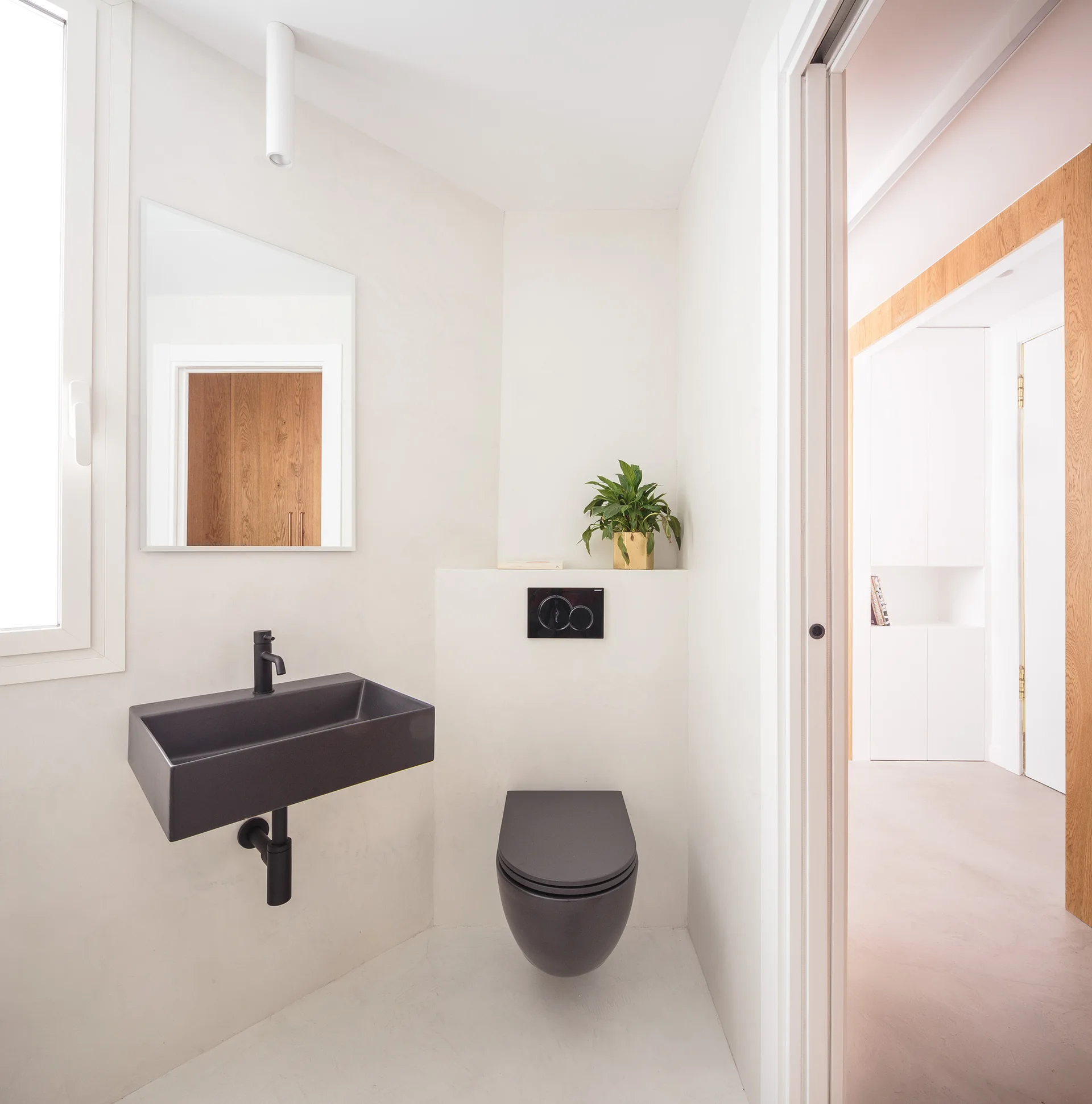A minimalist white powder room featuring a floating matte black sink, a wall-hung black toilet, and a frameless rectangular mirror.