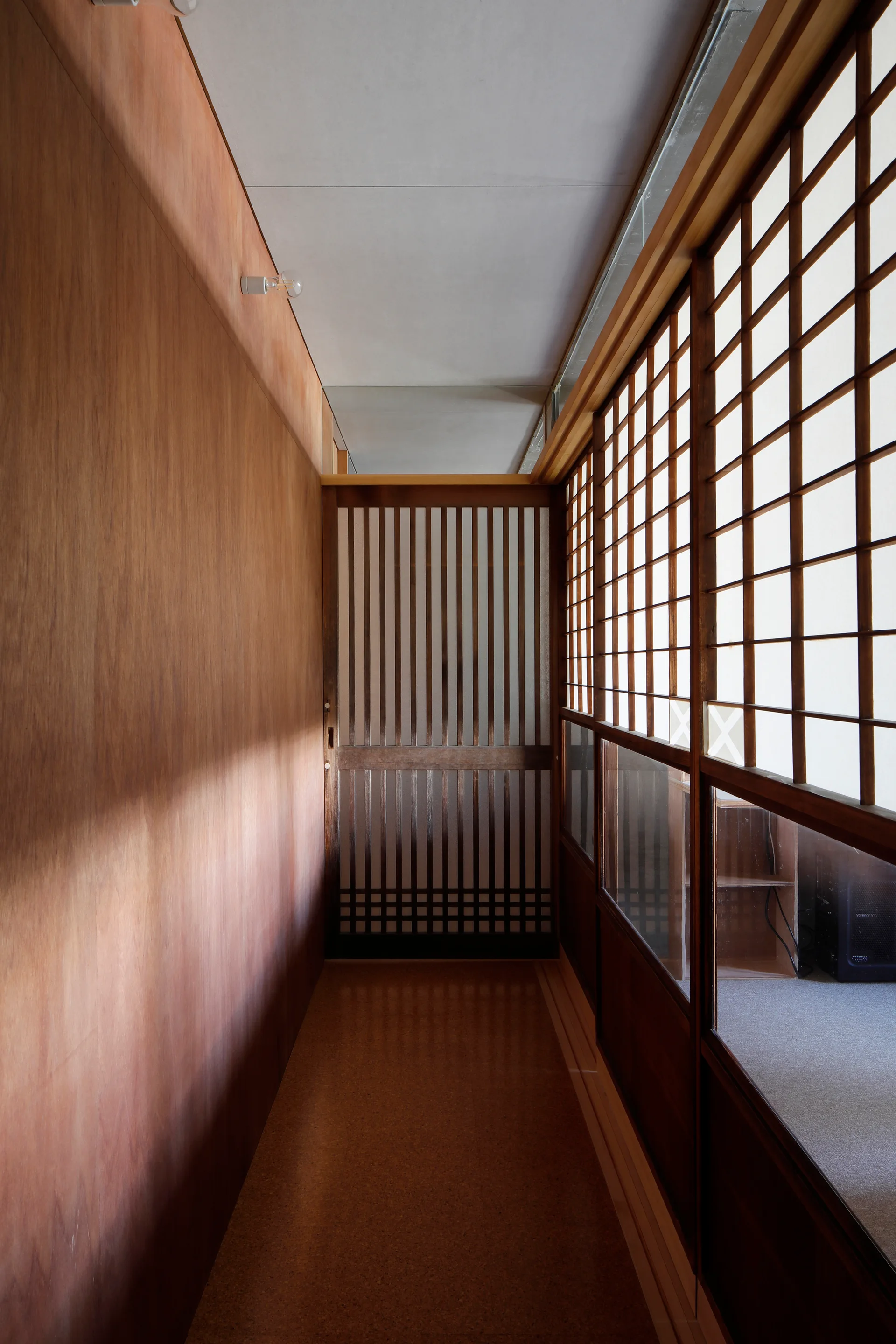 A narrow hallway features warm wood-paneled walls on one side and sliding wooden shoji screen doors with grid lattices on the other.