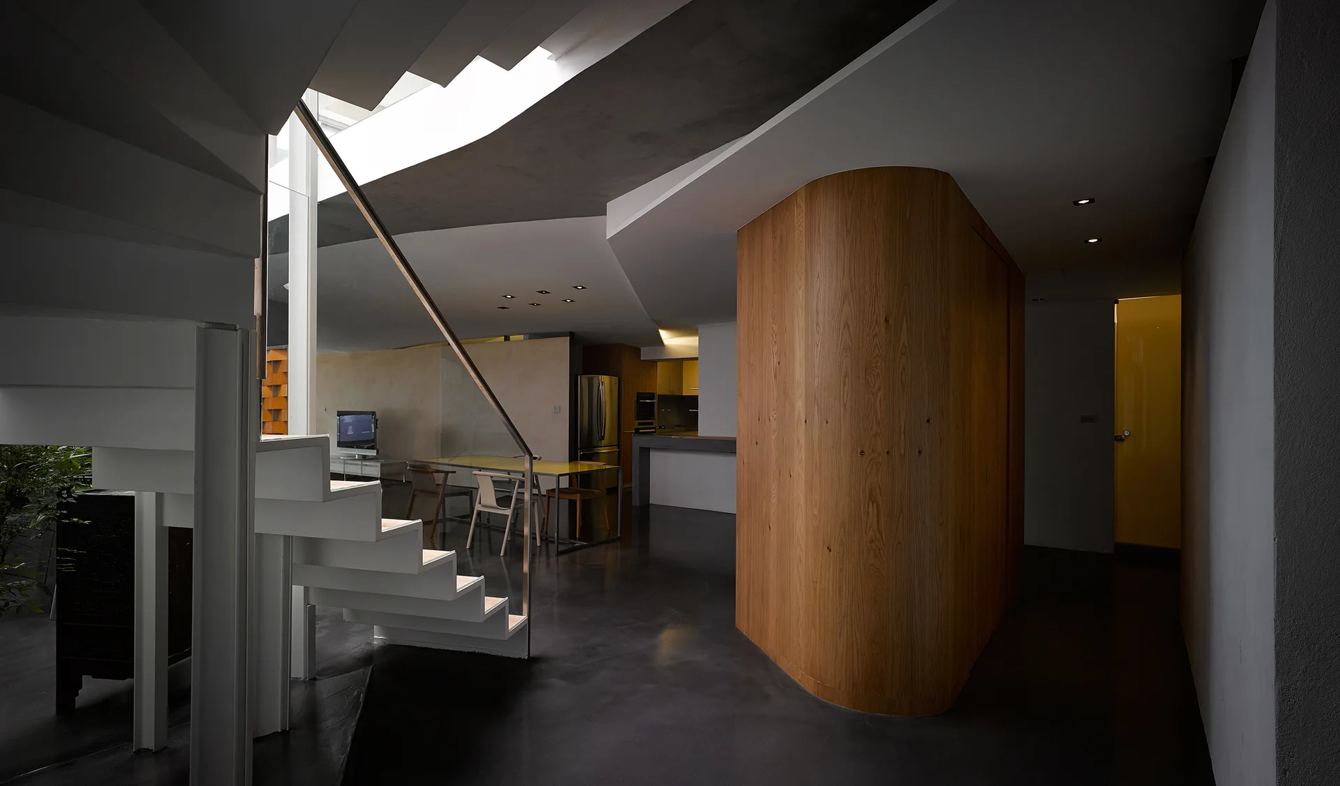 A modern interior features a white geometric staircase, a curved wood-paneled wall partition, and dark polished flooring.