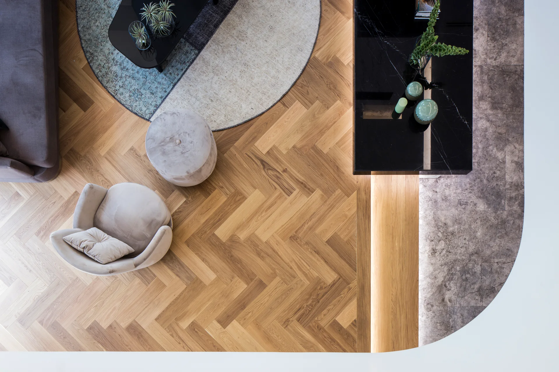 Overhead view of a contemporary living room with herringbone wood floors, a circular rug, a grey armchair, and a black marble console.