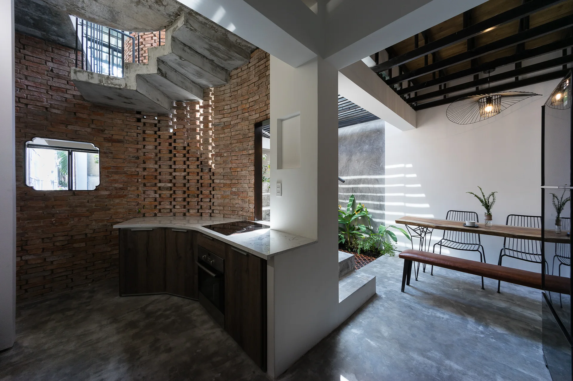 An open-concept kitchen and dining area featuring a curved red brick wall, concrete floors, and a sculptural concrete staircase.