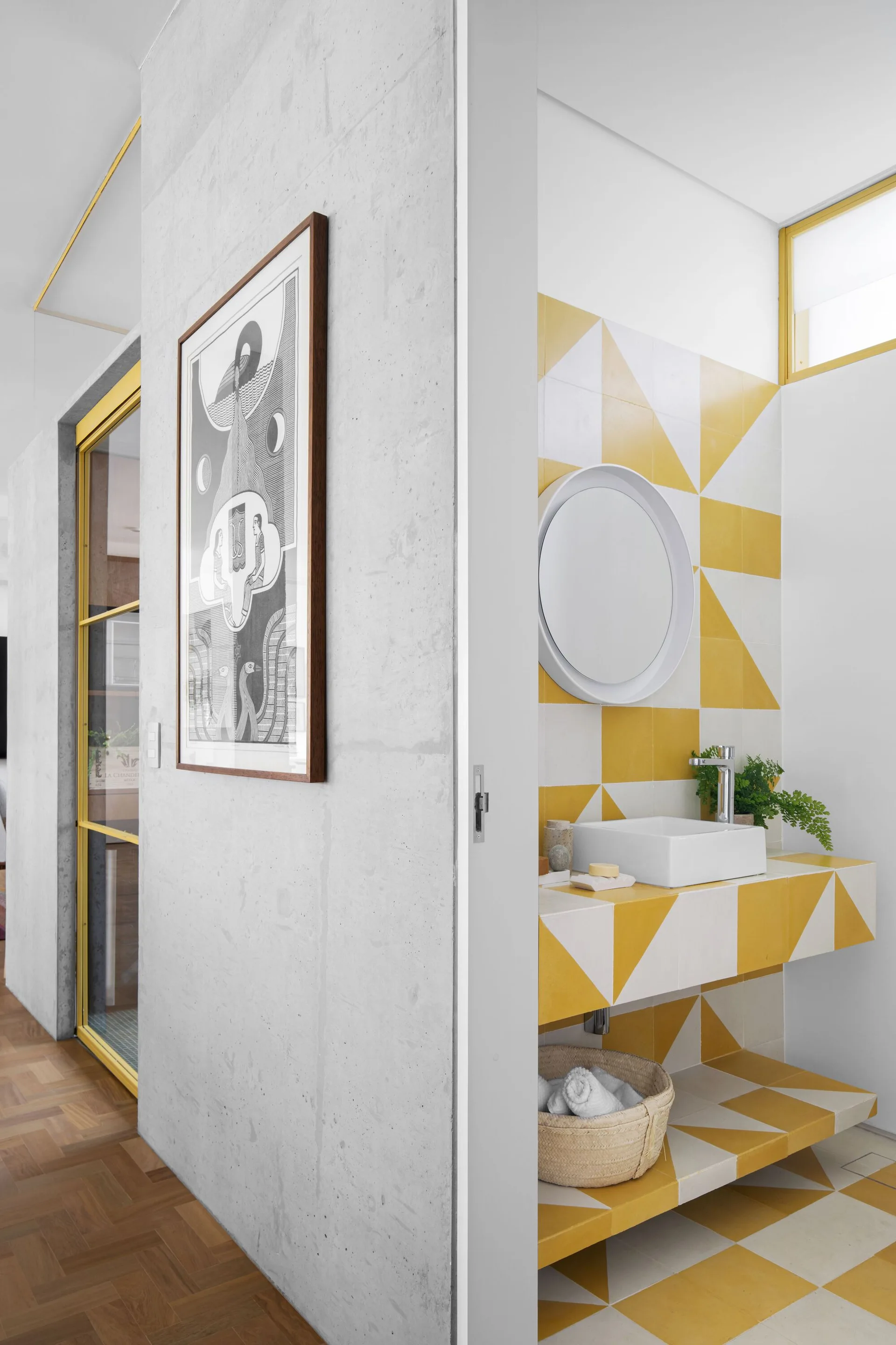 A modern powder room features a white vessel sink on a floating vanity covered in yellow and white geometric tiles next to a concrete wall.