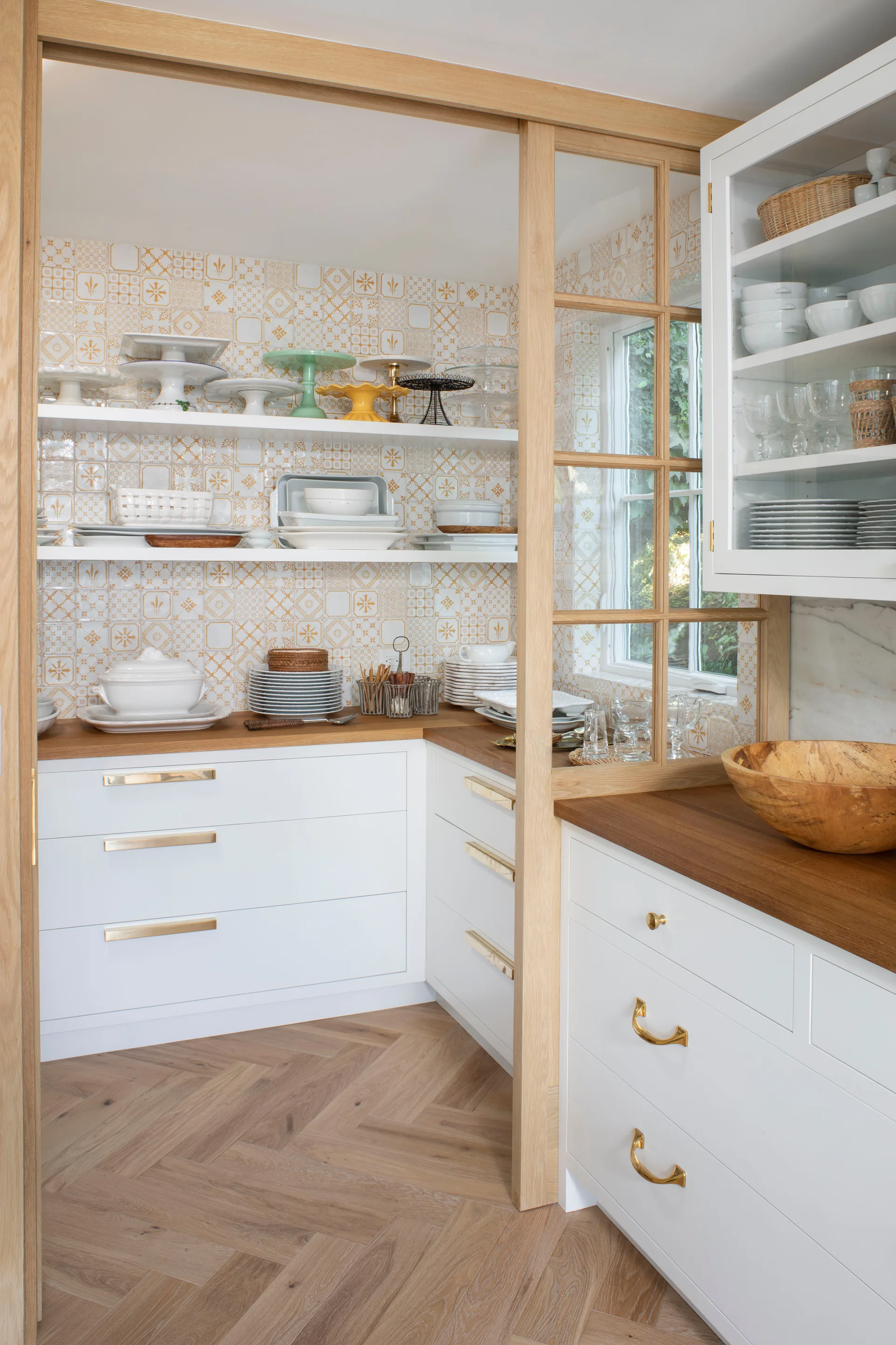 A walk-in pantry features white cabinets with wood countertops, yellow patterned wall tile, open shelves, and a sliding oak glass door.