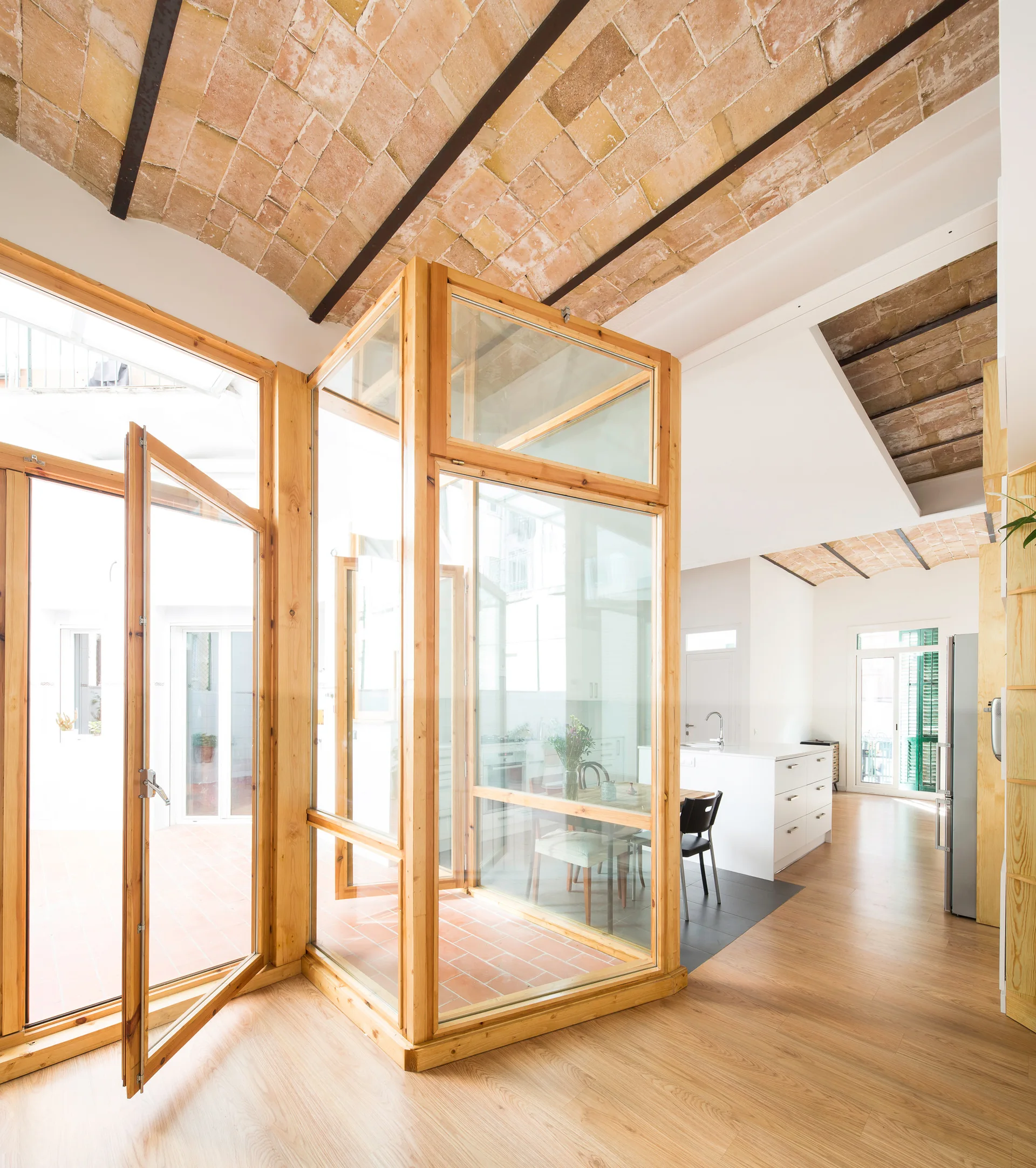 An open kitchen with a vaulted brick ceiling features a central wood and glass enclosure, a white island, and wood floors.