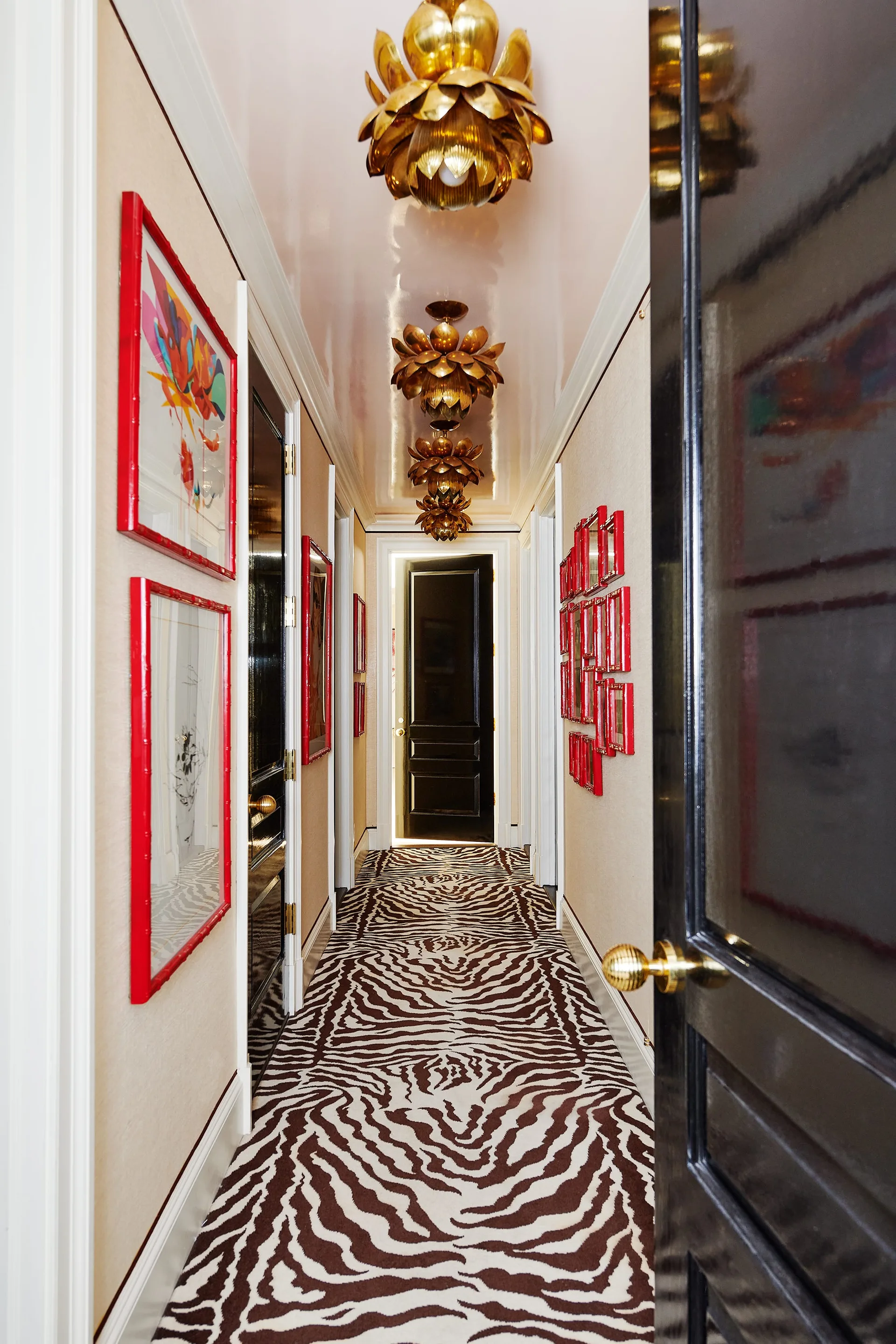 A long hallway features a zebra-patterned runner rug, high-gloss black doors, gold flower-shaped ceiling lights, and red picture frames on beige walls.