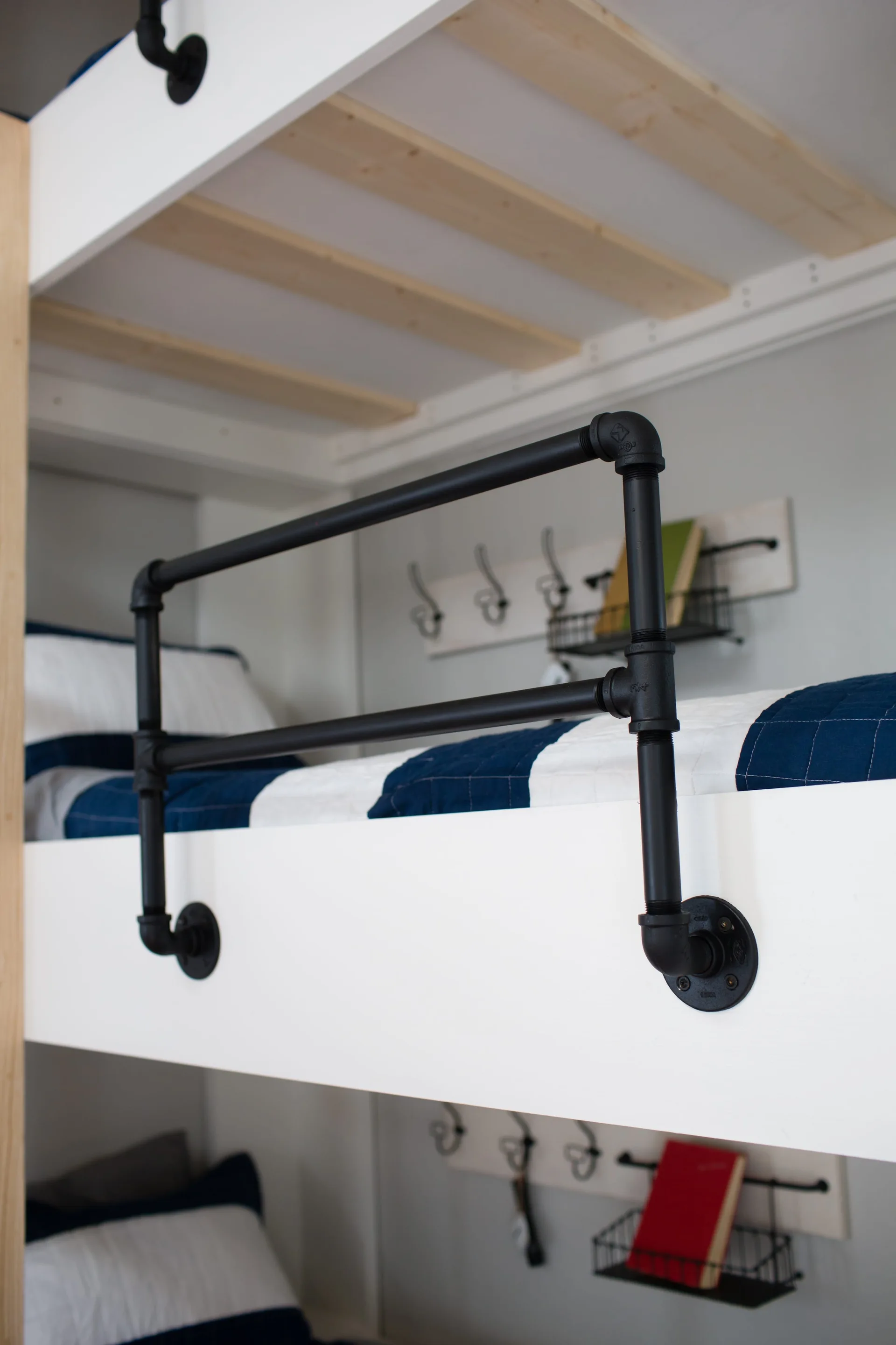 A white wooden bunk bed features a matte black industrial pipe guardrail and blue and white striped quilted bedding.