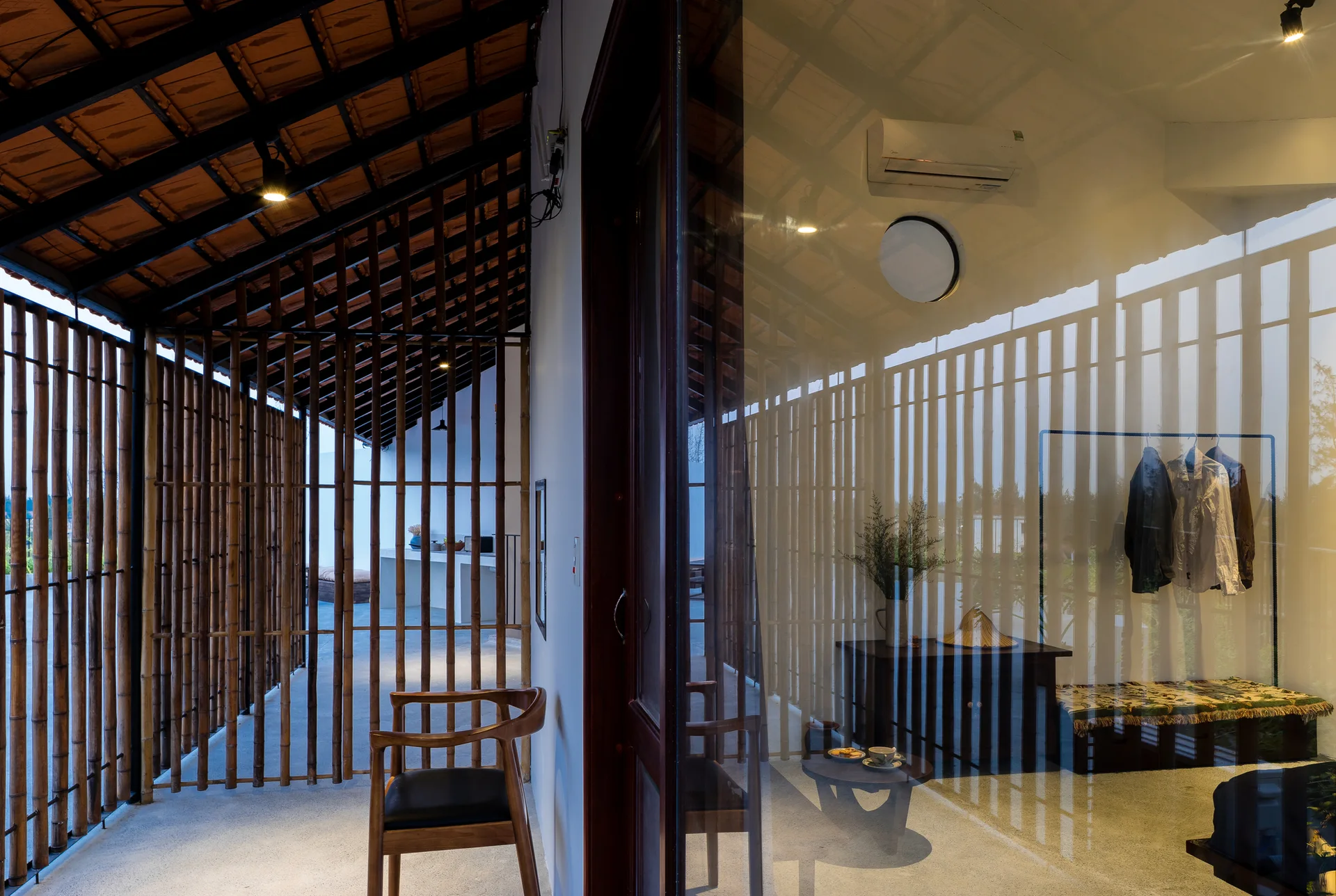 A transitional entryway features a vertical bamboo screen wall, a wooden armchair, and a glass partition reflecting the interior.