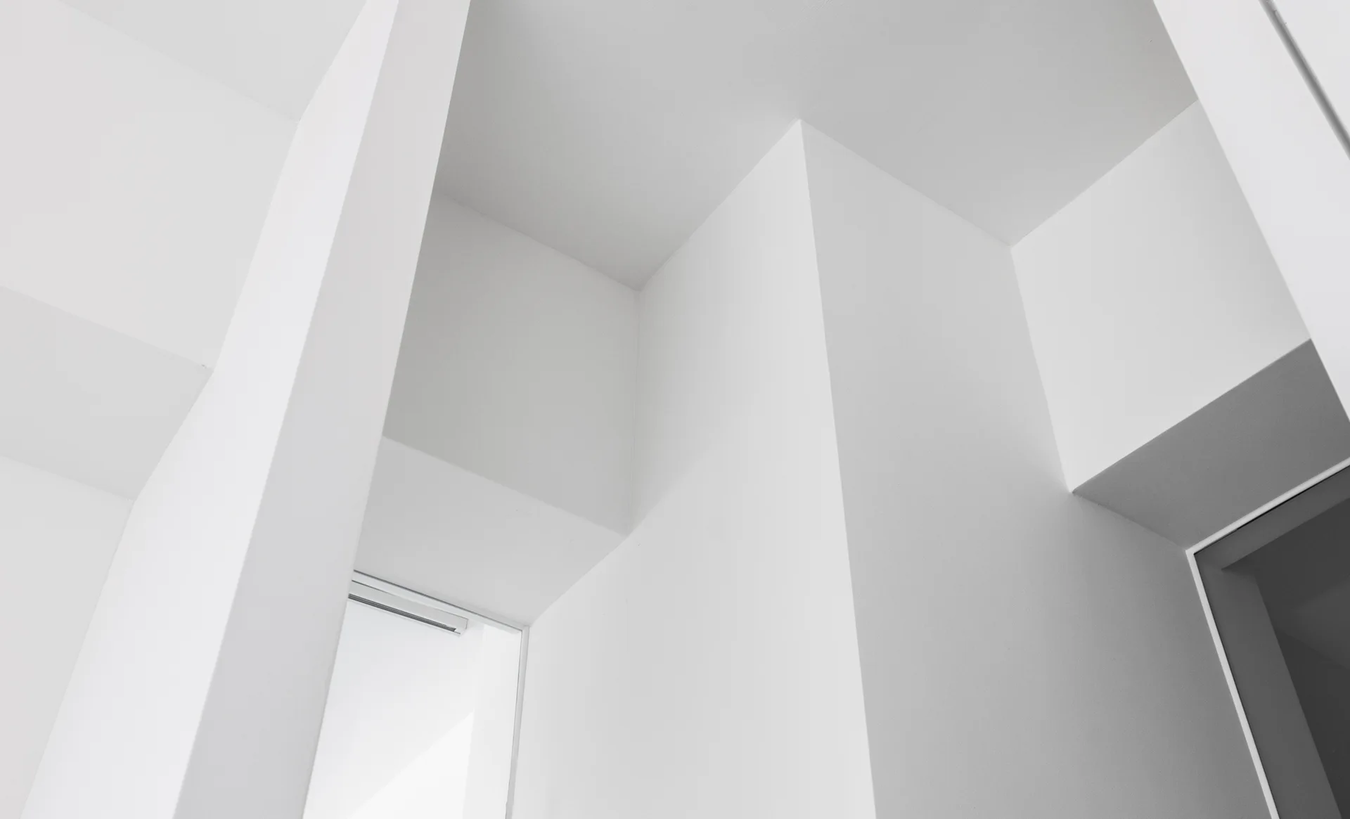 Intersecting matte white walls and ceilings create sharp geometric angles and soft shadowed recesses in a minimalist interior.