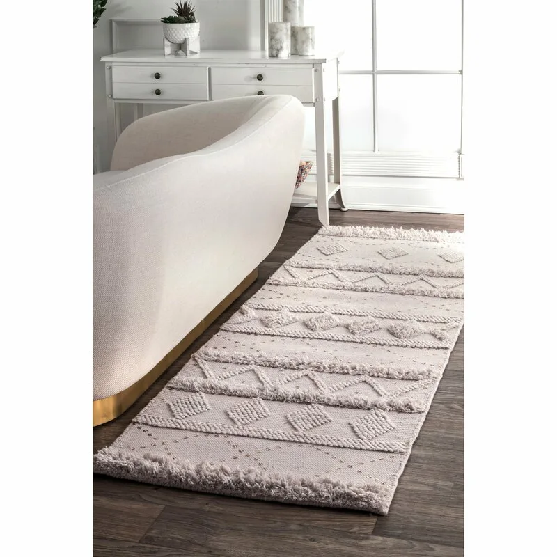 A textured cream runner rug with a tufted geometric pattern sits on a dark hardwood floor next to a curved beige sofa.