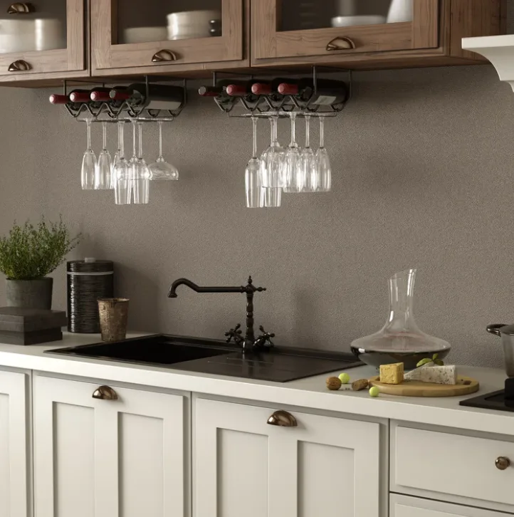 A kitchen counter features white base cabinets, a black sink, upper wood cabinets, and two metal wine racks hanging underneath holding glasses and bottles.