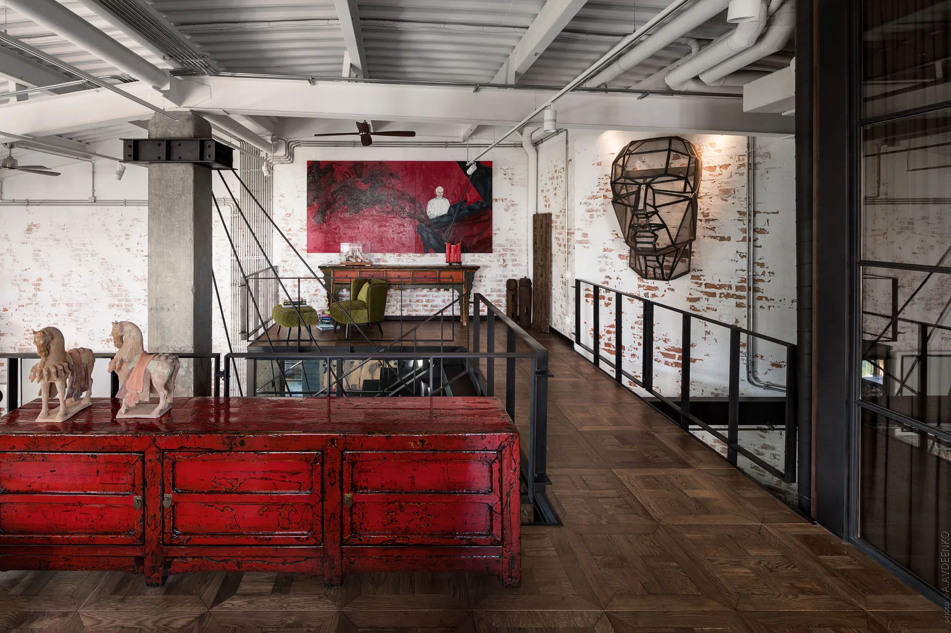 An industrial loft featuring a red lacquer console table, dark parquet flooring, black railings, and white painted brick walls.
