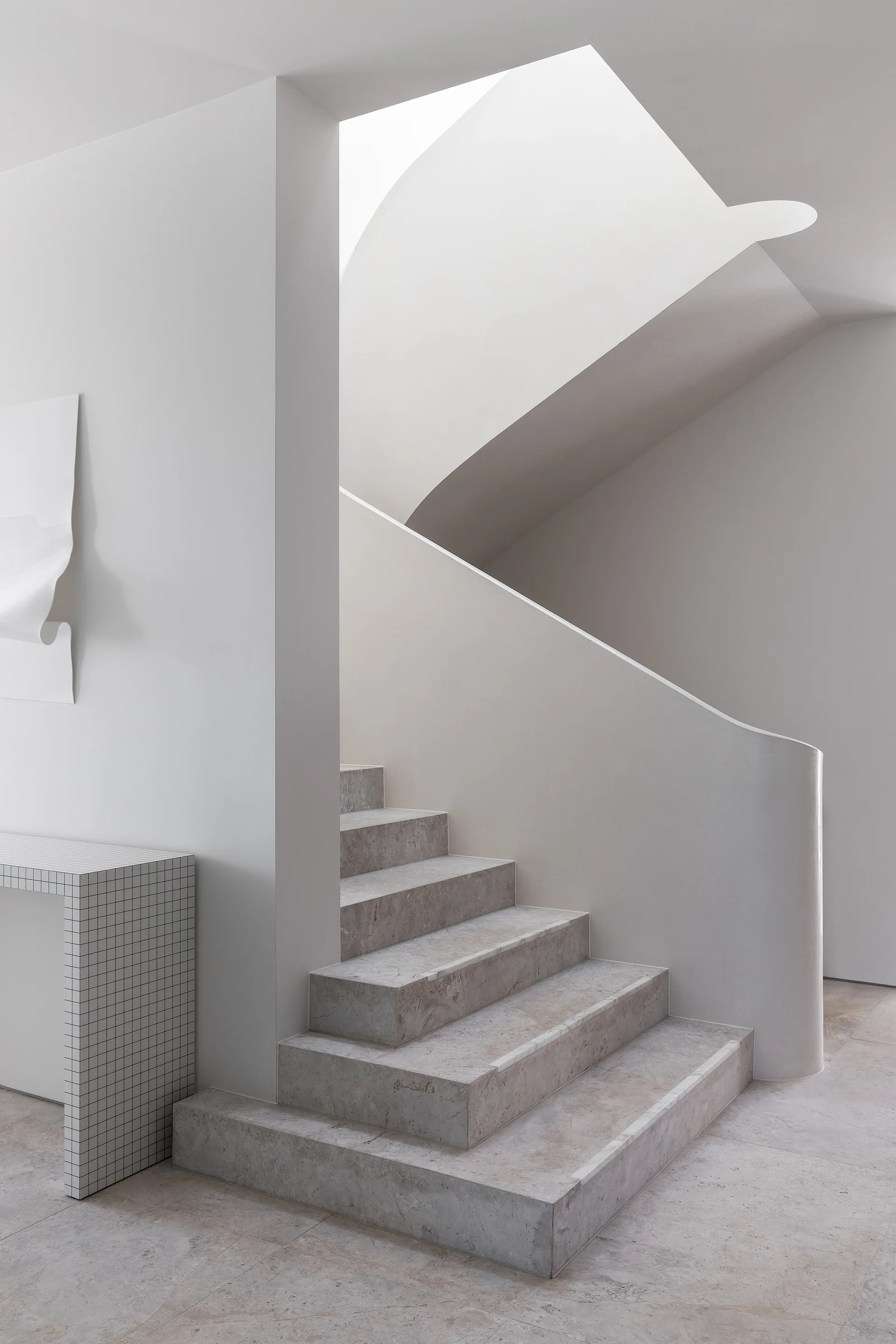 A minimalist interior featuring a stone staircase with curved plaster walls and a grid patterned console table.