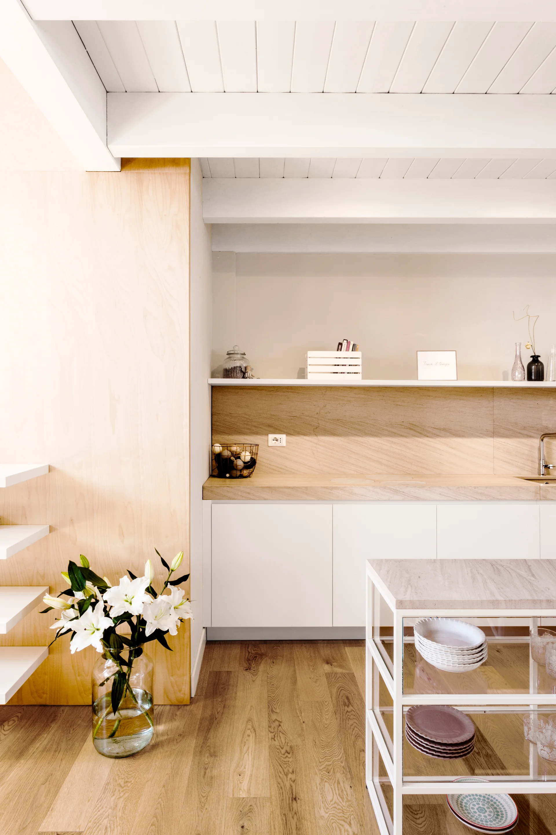 A bright kitchen features white cabinets, a light wood countertop, a plywood wall panel, and an open-frame kitchen island under a beamed ceiling.