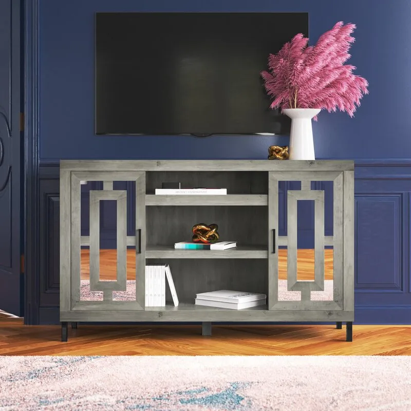 A gray wooden media cabinet with geometric glass doors sits against a navy blue paneled wall beneath a mounted television.