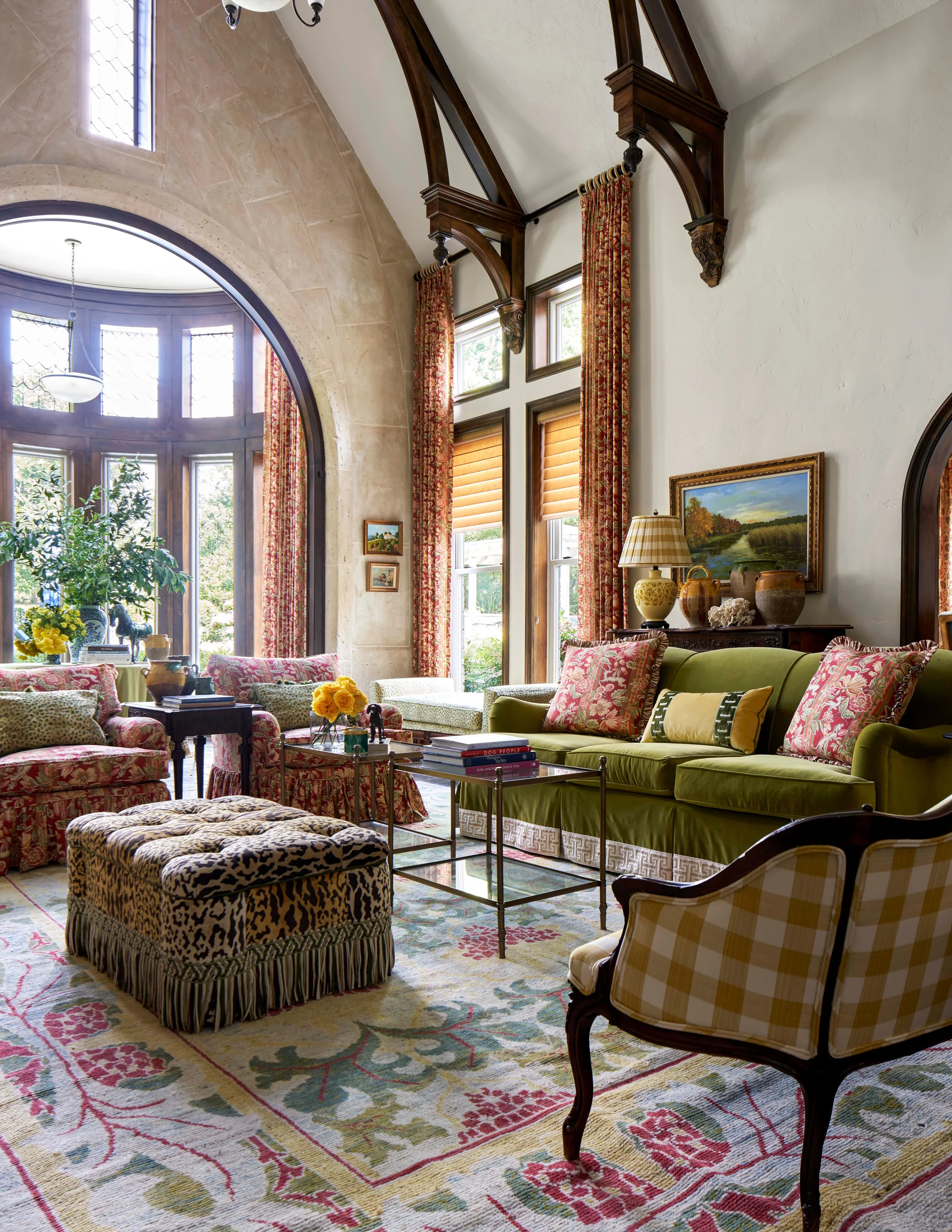 A grand living room features a vaulted ceiling with dark wood beams, an olive green velvet sofa, and a leopard print upholstered ottoman.