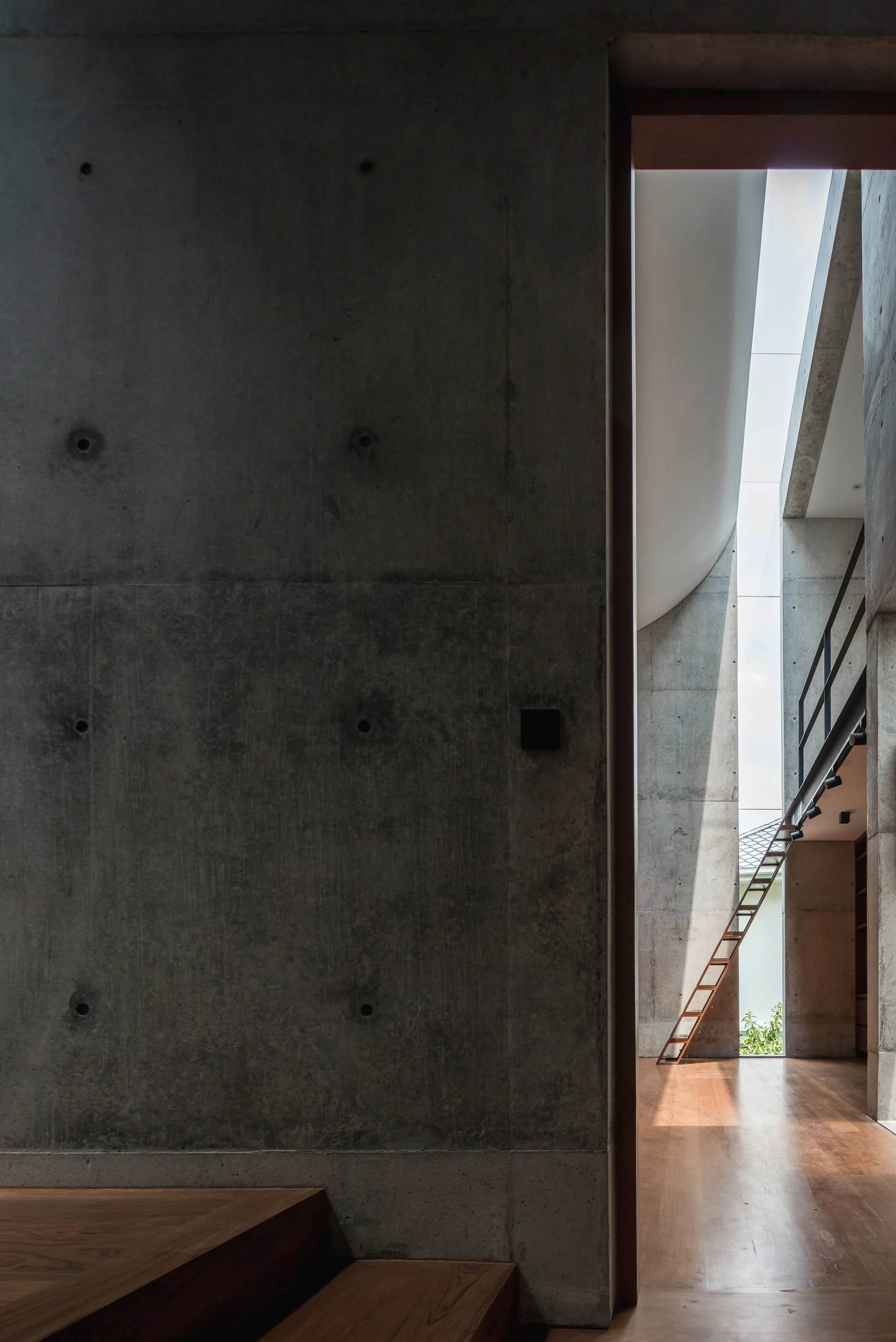 An interior view looking through a concrete doorway into a tall space with exposed concrete walls, hardwood floors, and a vertical light well.