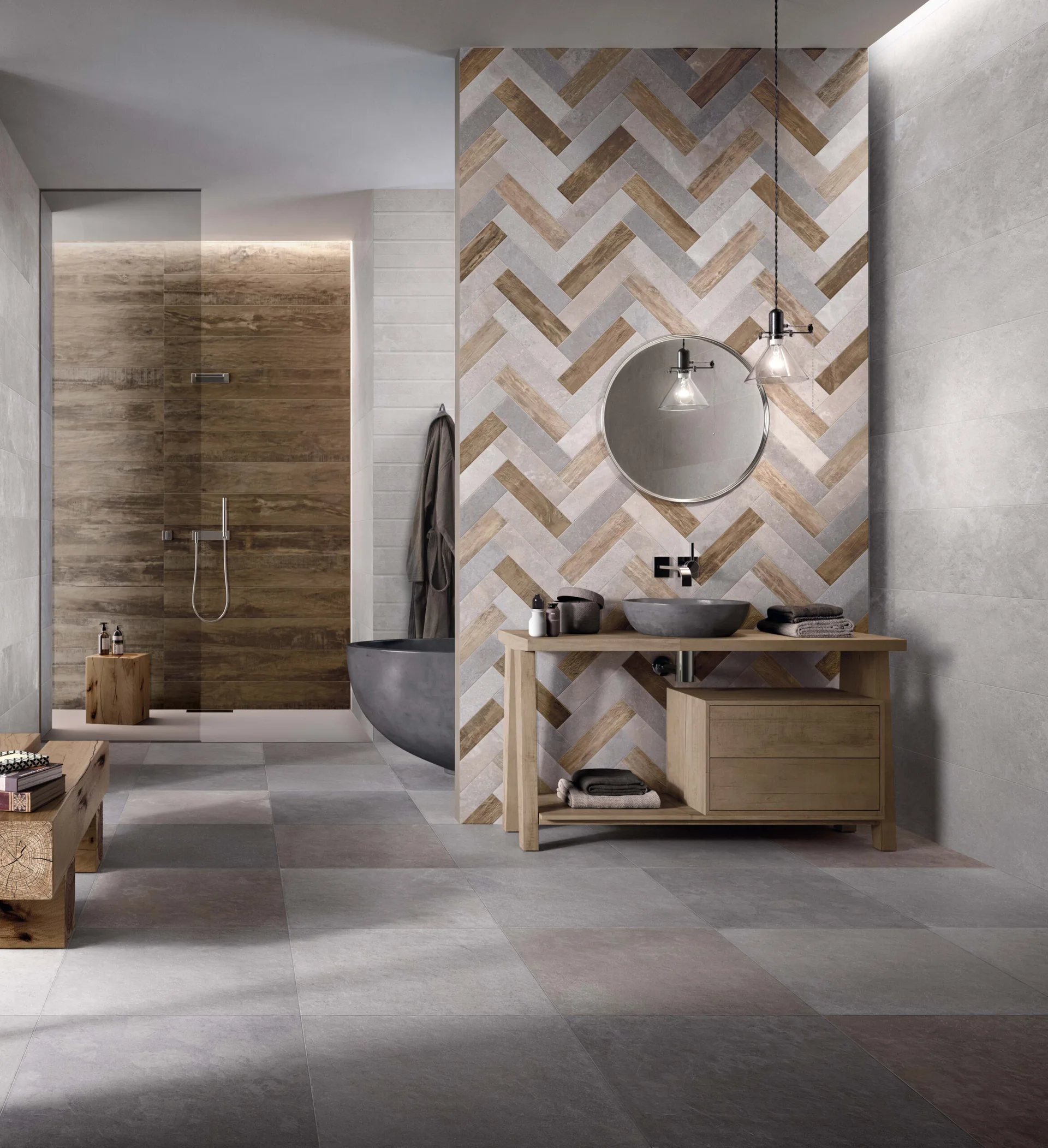 A modern bathroom features a mixed-texture herringbone tile wall, a wooden vanity with a stone basin, and a grey sculptural bathtub.