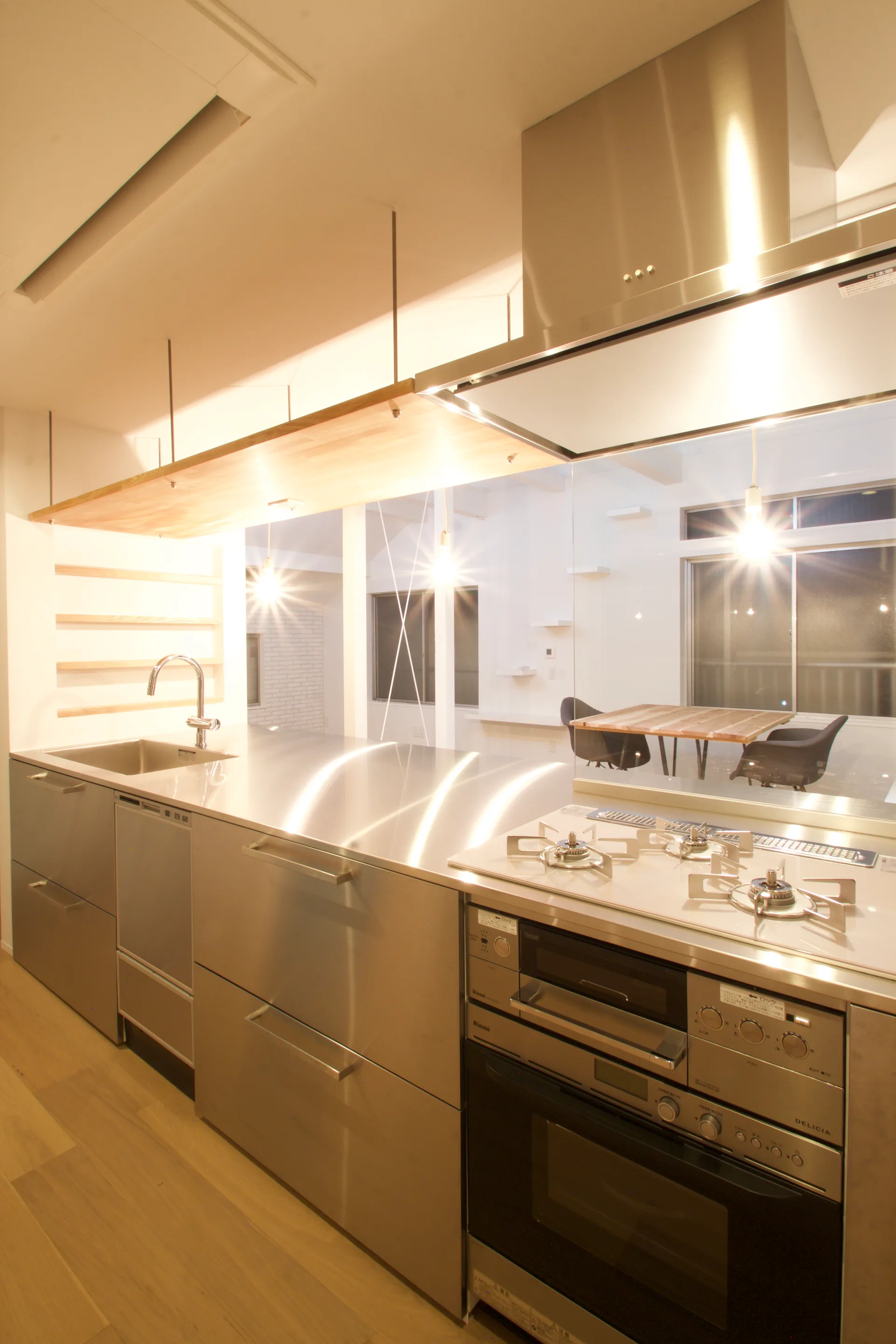 A modern kitchen with a stainless steel island, an integrated gas stove, and a suspended light wood shelf under warm lighting.