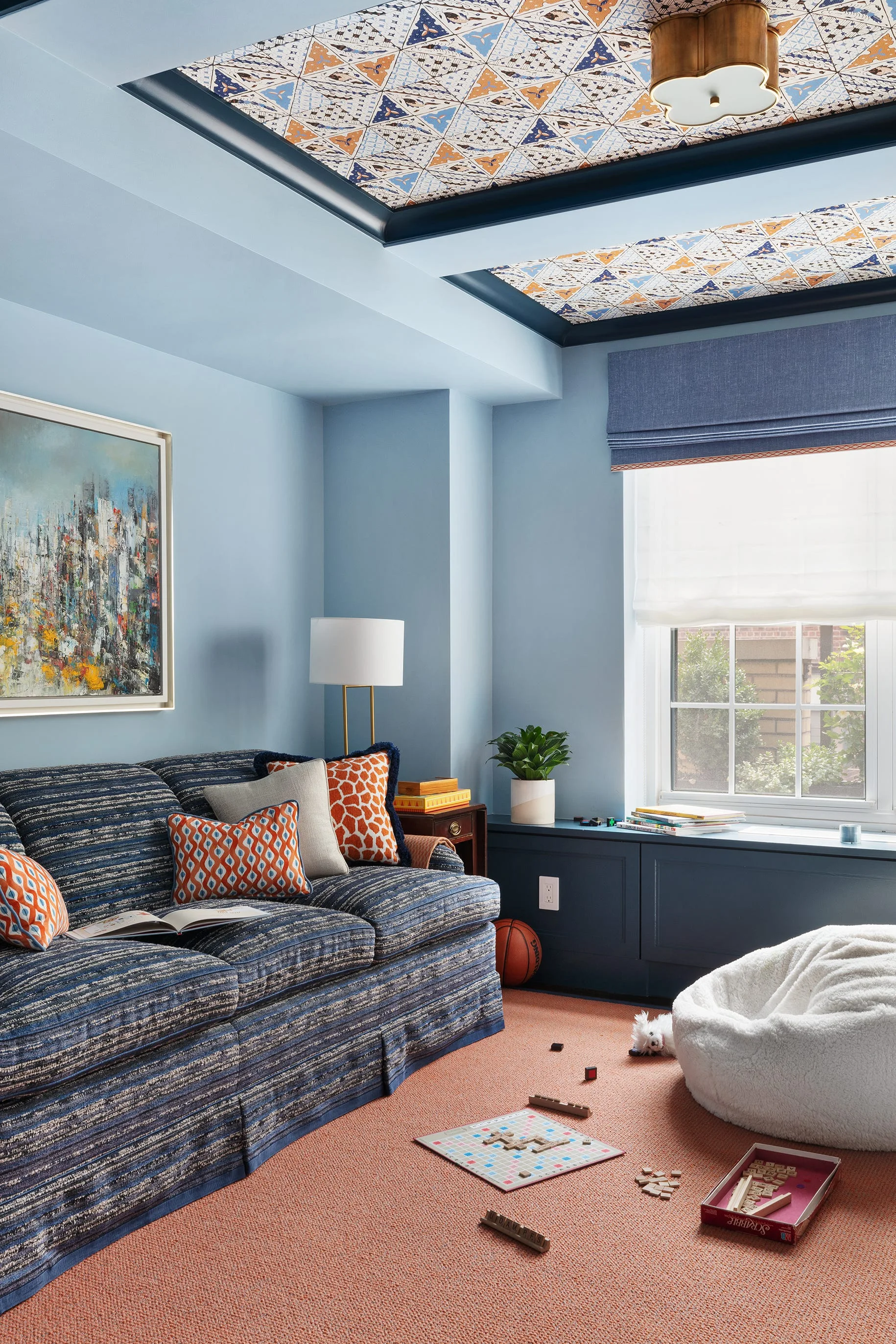 A blue family room features a striped sofa, a patterned tray ceiling, a white bean bag, and coral-colored carpeting.