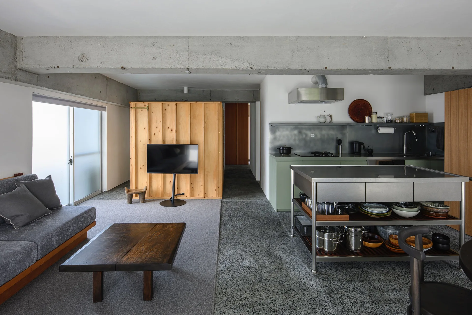 An open-plan residential interior with an industrial kitchen featuring a stainless steel island next to a living area with a grey sofa.
