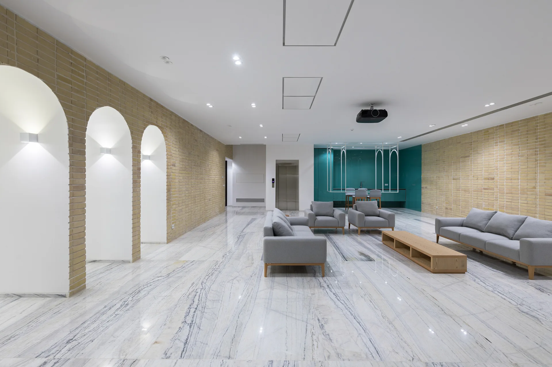 A spacious modern lounge featuring polished grey-veined marble flooring, light brick walls with arched niches, and grey sofas.