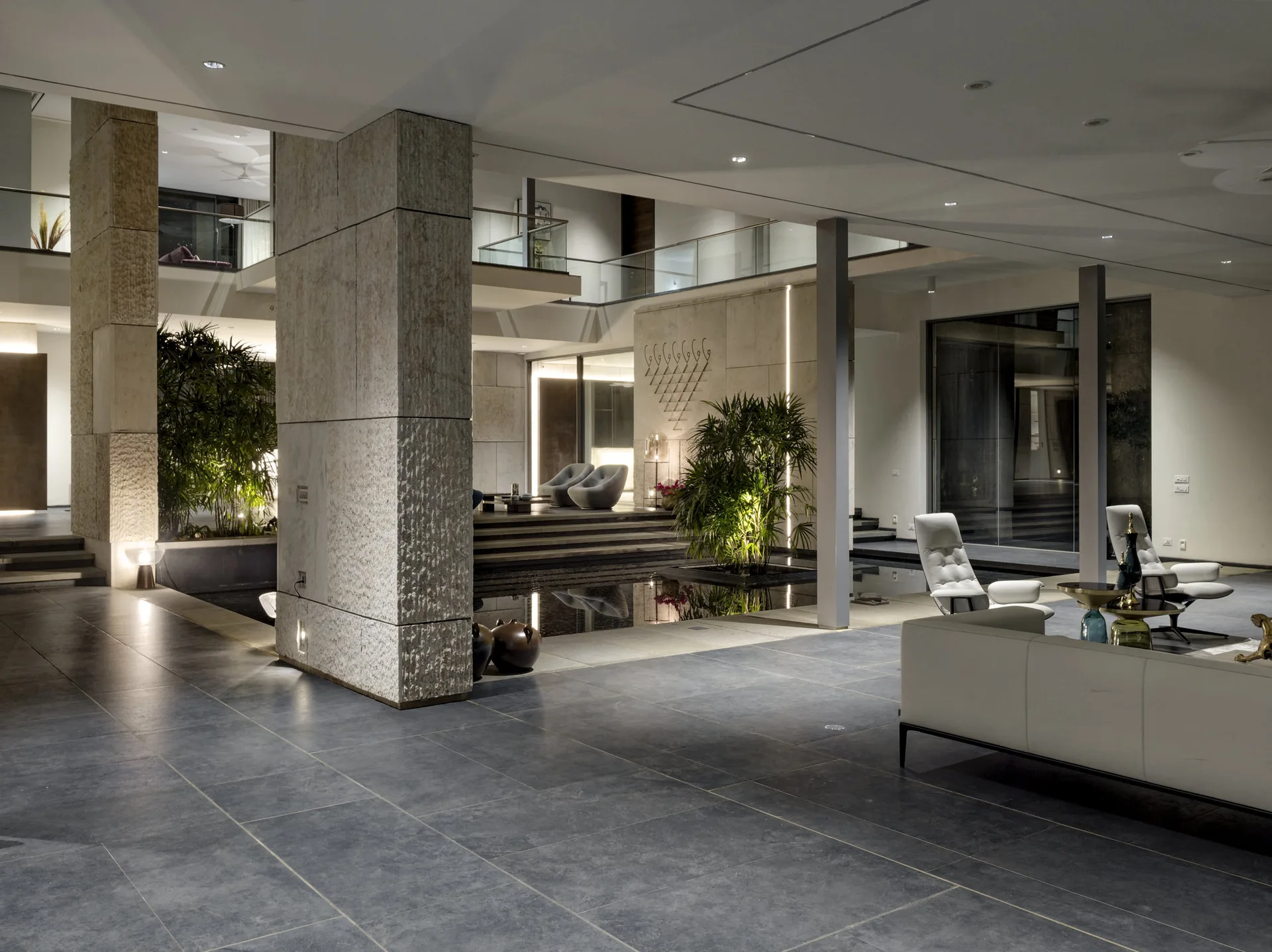 A spacious open-concept living area with large textured stone pillars, a shallow indoor reflection pool, and minimalist white seating.