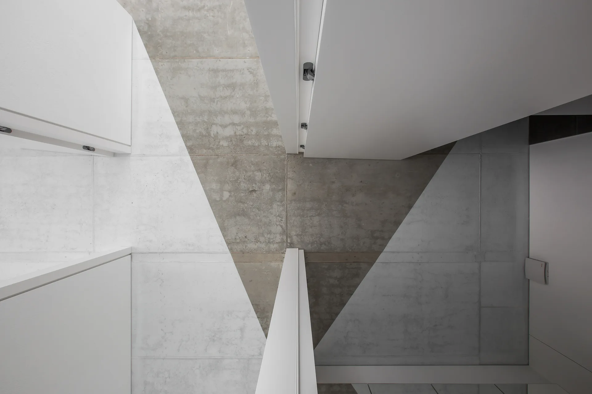 Matte white minimalist doors intersect with a textured gray concrete ceiling in a sharp geometric composition.