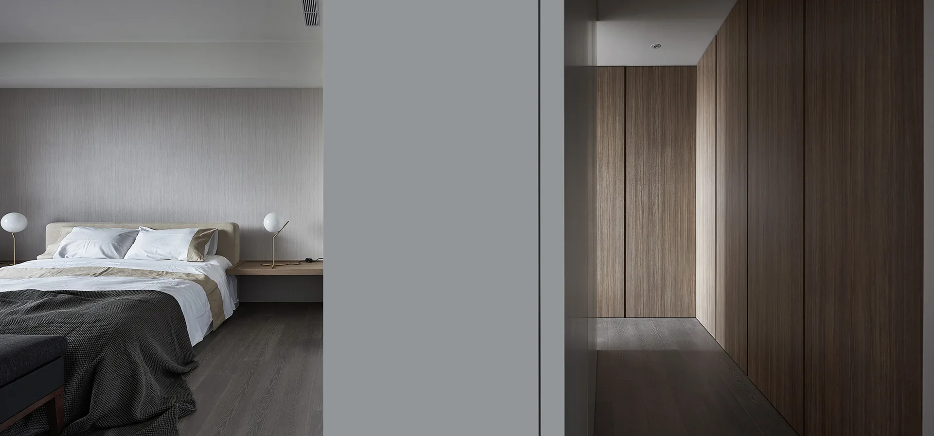 A minimalist bedroom features an upholstered bed, spherical bedside lamps, grey wood flooring, and a hallway lined with tall wood closet cabinets.