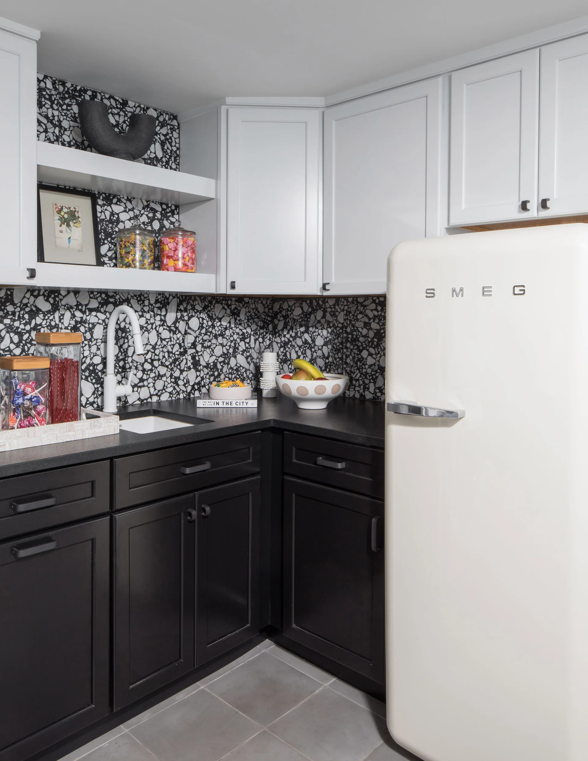 A kitchen corner featuring black shaker base cabinets, white upper cabinets, a terrazzo backsplash, and a cream retro refrigerator.