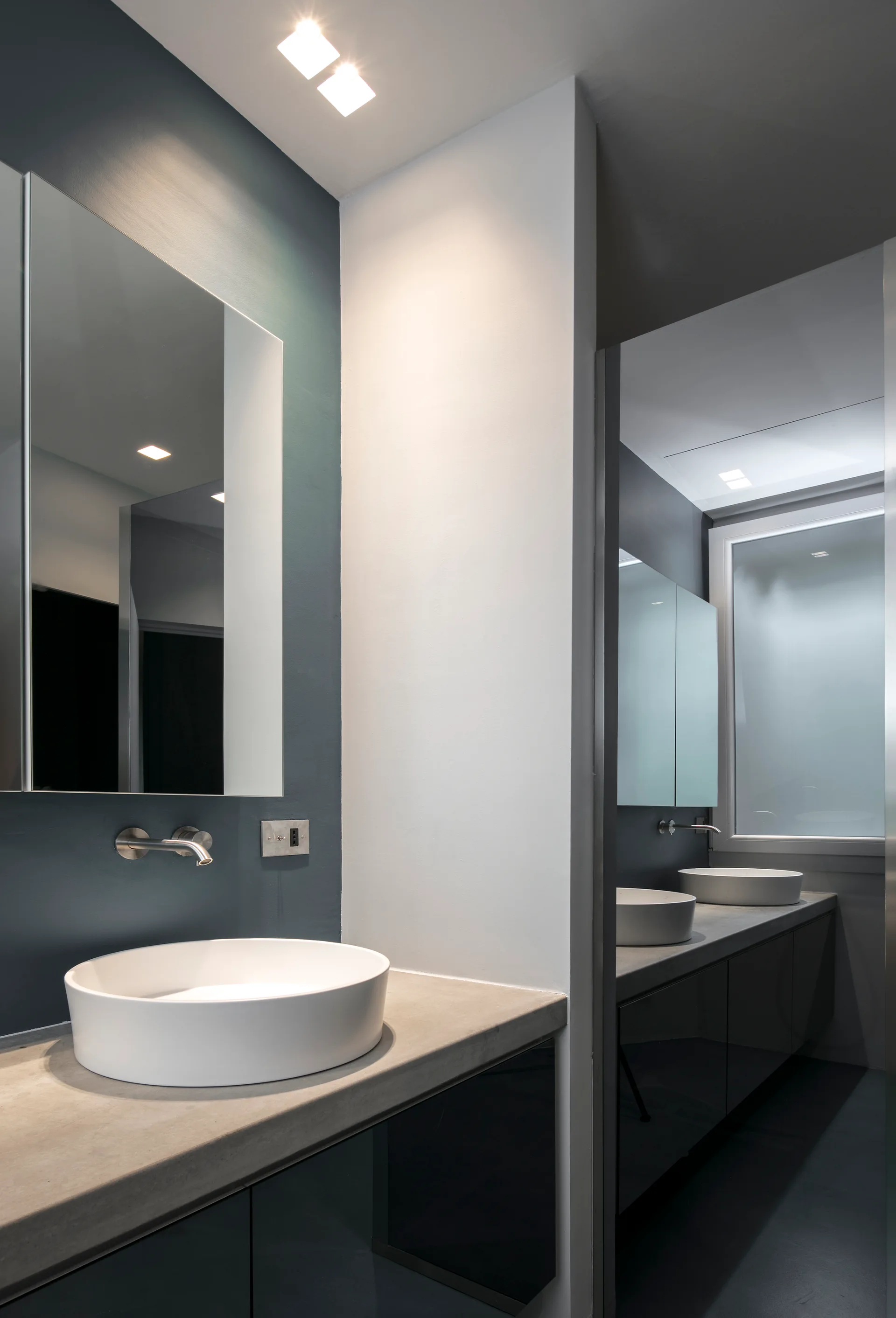 A modern bathroom vanity features a round white vessel sink on a matte concrete countertop against a dark blue accent wall.